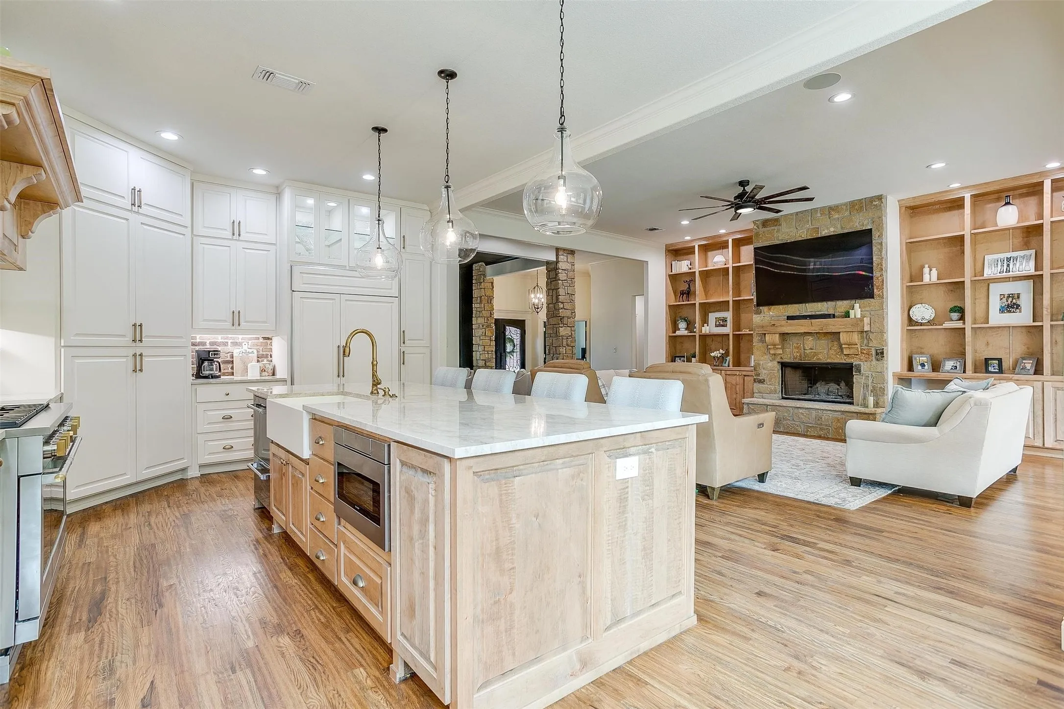 Kitchen with a stone fireplace, built in features, open floor plan, light stone counters, and dual tone cabinetry