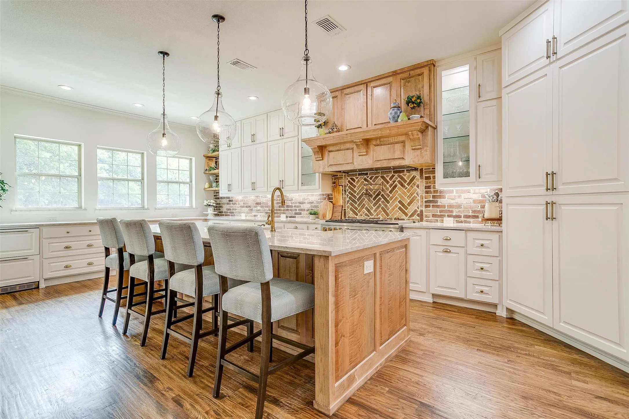 Kitchen featuring glass fronted cabinets, open shelves, light stone counters, a kitchen island with sink, and pendant lighting