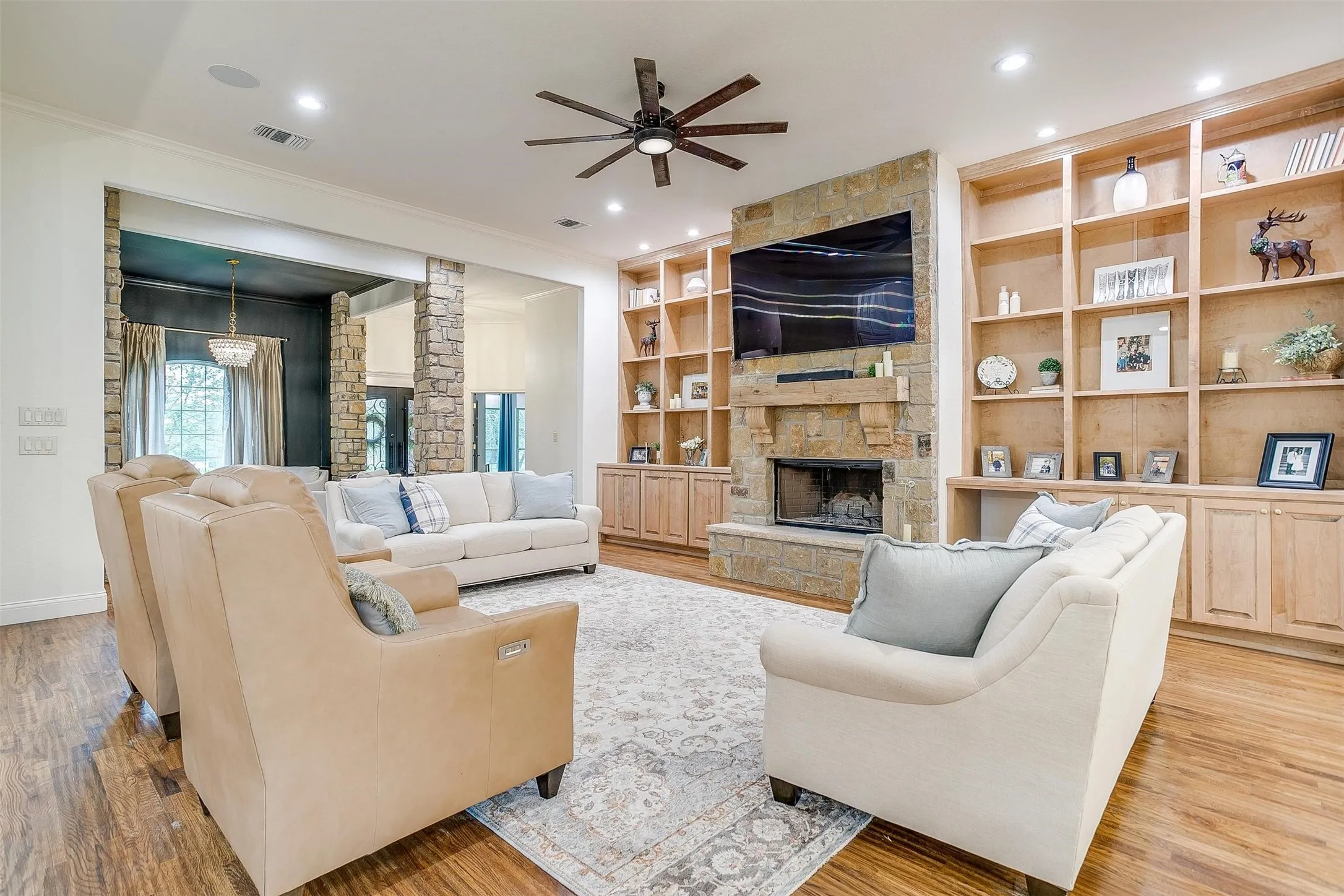 Living area featuring a stone fireplace, built in shelves, ceiling fan, light wood-style flooring, and crown molding