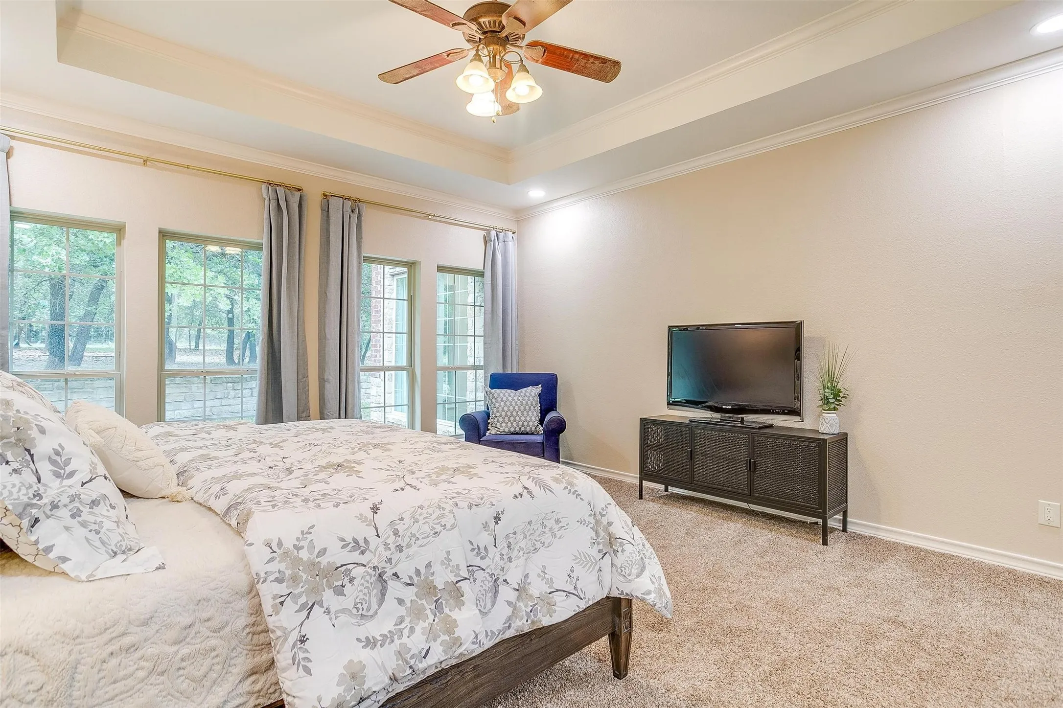 Bedroom with a tray ceiling, light colored carpet, ceiling fan, and crown molding