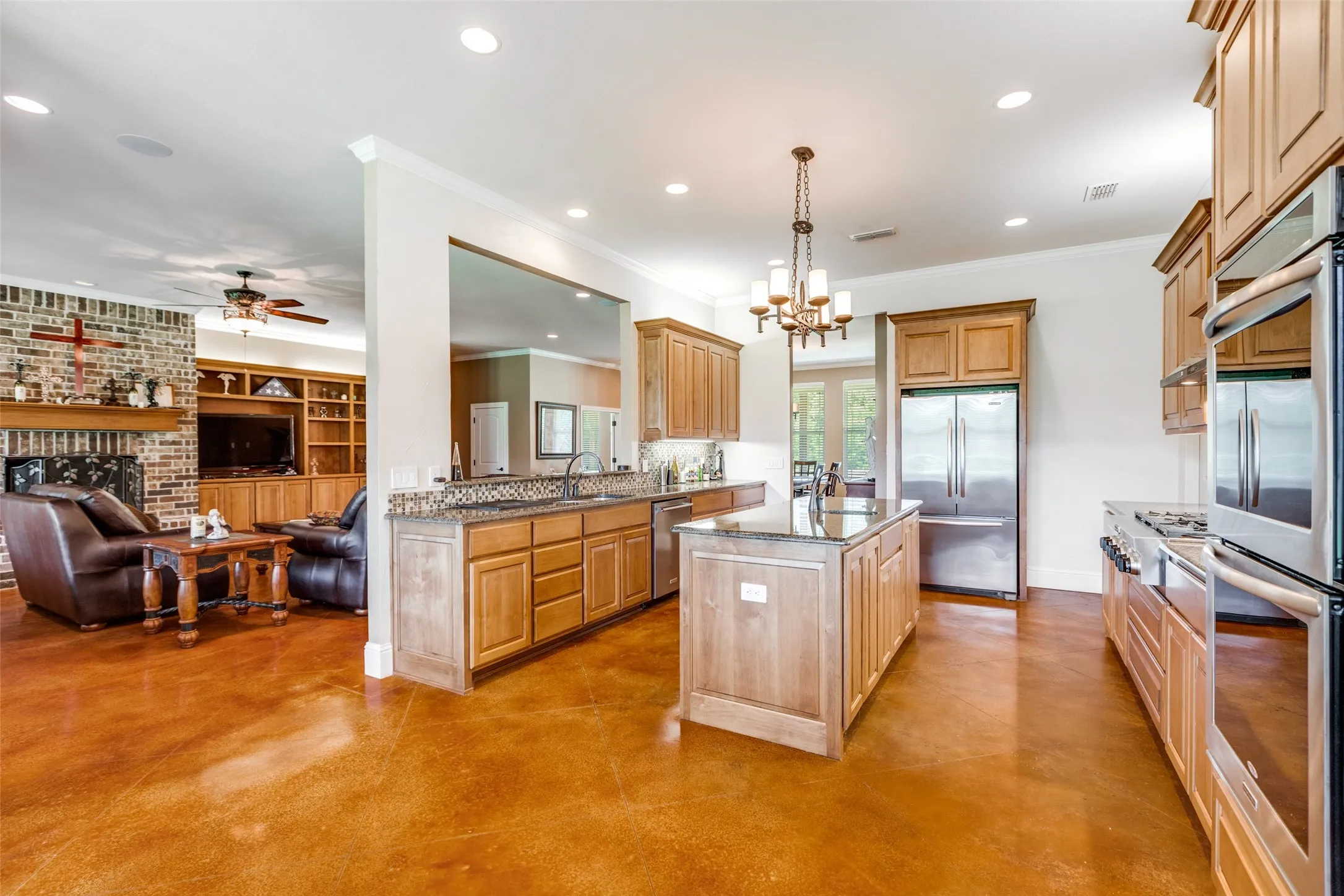 Kitchen featuring a kitchen island with sink, light stone counters, stainless steel appliances, open floor plan, and concrete flooring