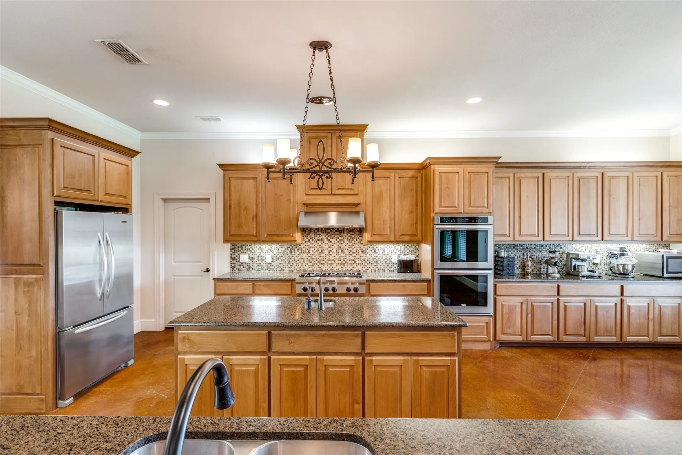 Kitchen with stainless steel appliances, tasteful backsplash, ornamental molding, dark stone countertops, and brown cabinets