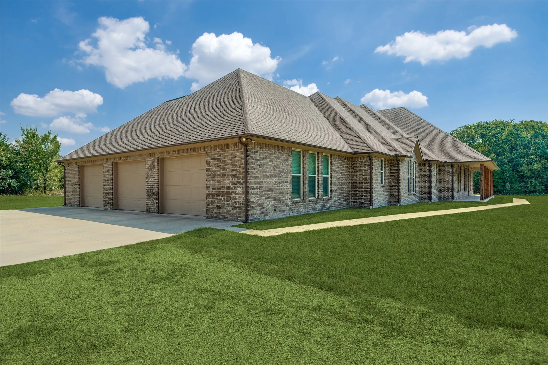 View of front of house featuring a shingled roof, brick siding, a front lawn, and driveway