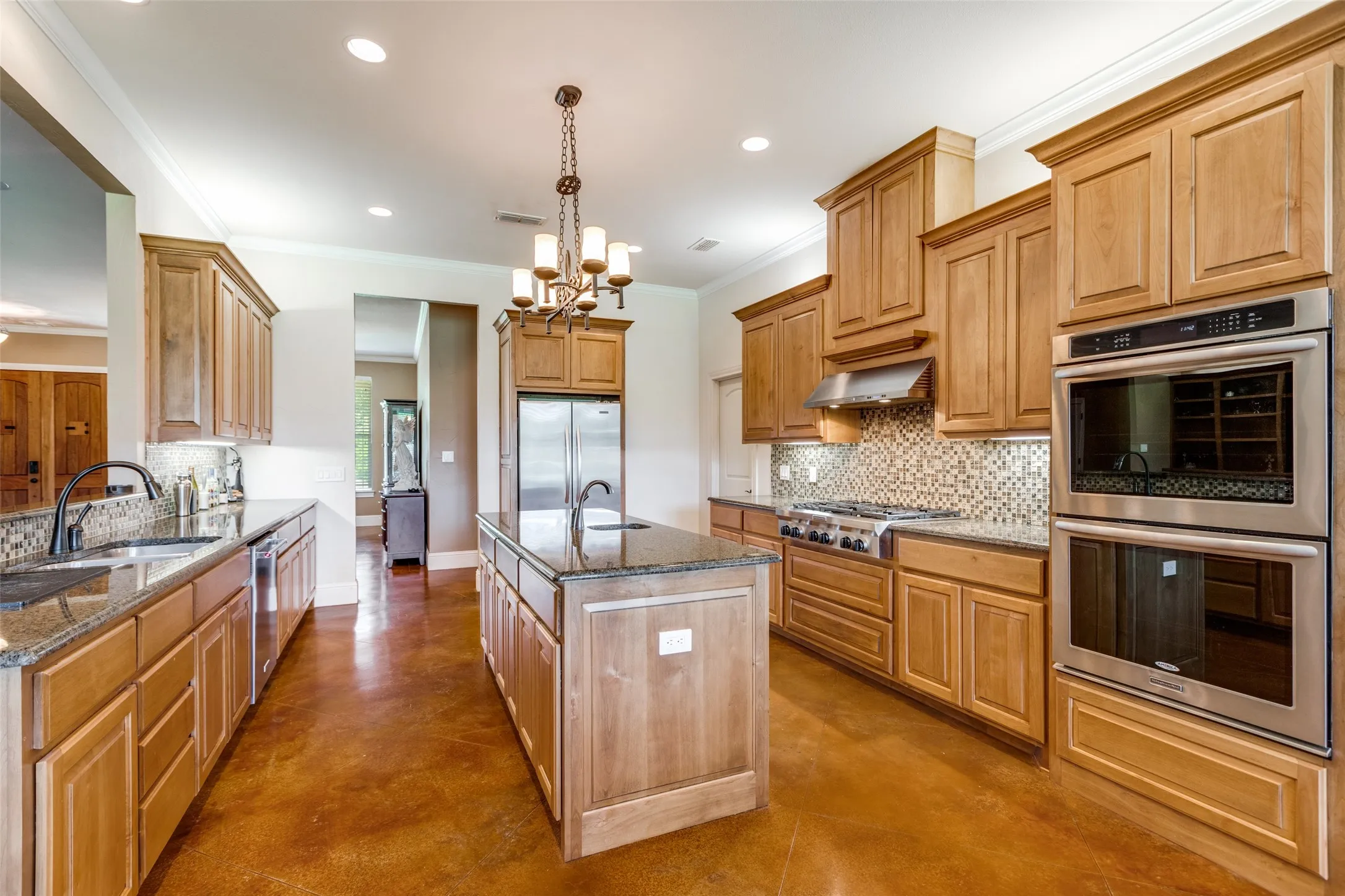 Kitchen featuring tasteful backsplash, appliances with stainless steel finishes, concrete floors, ornamental molding, and dark stone counters