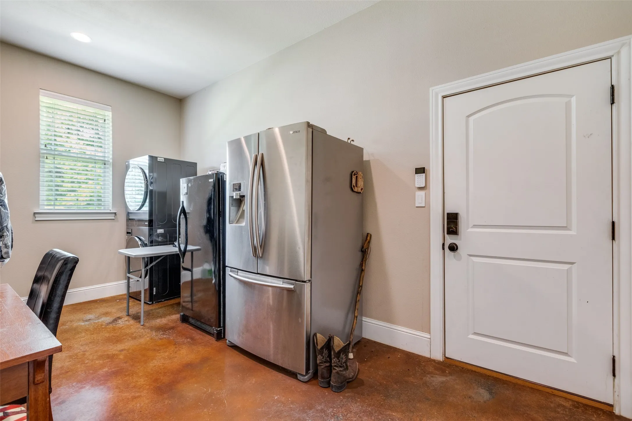 Kitchen featuring stainless steel fridge, concrete flooring, freestanding refrigerator, and estacked washer and dryer