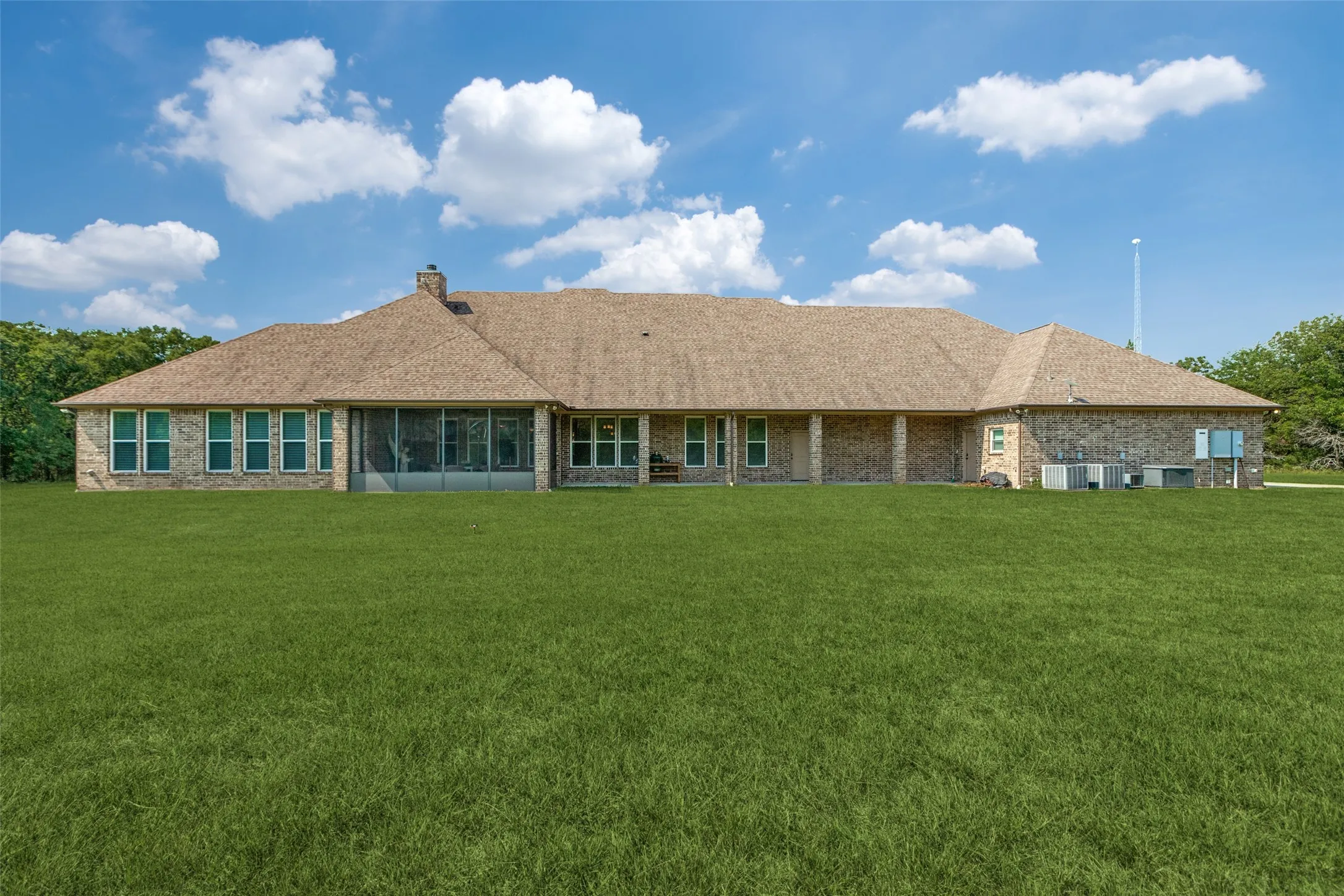 Rear view of house featuring a yard, roof with shingles, brick siding, and a chimney