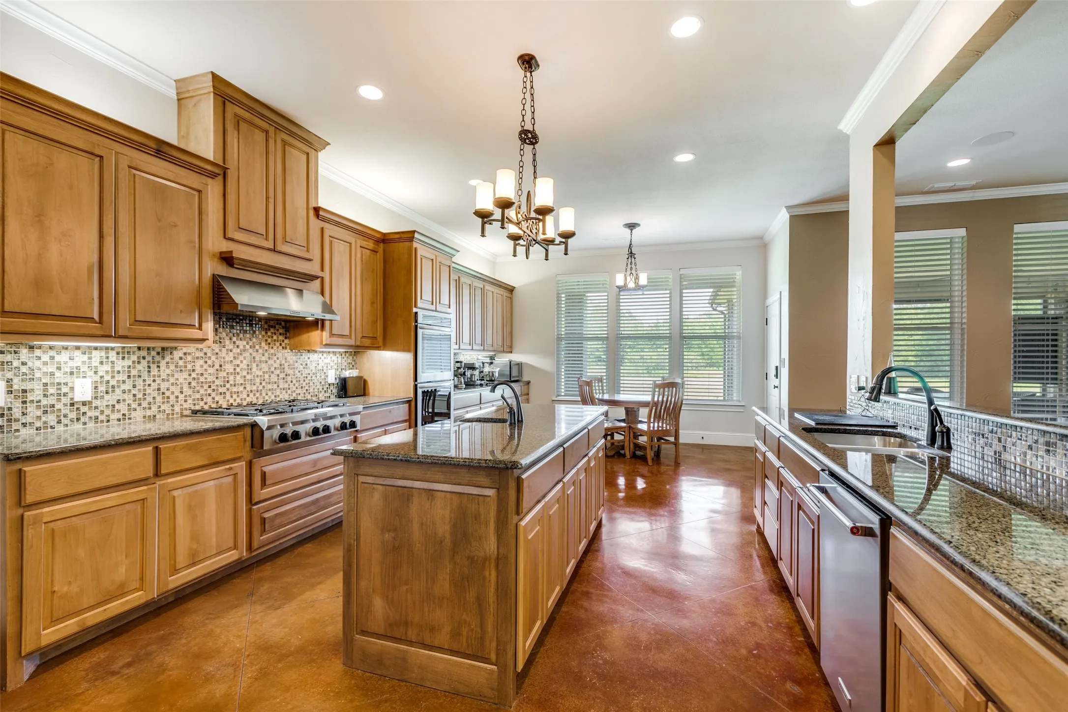 Kitchen featuring backsplash, ornamental molding, dark stone countertops, brown cabinetry, and decorative light fixtures