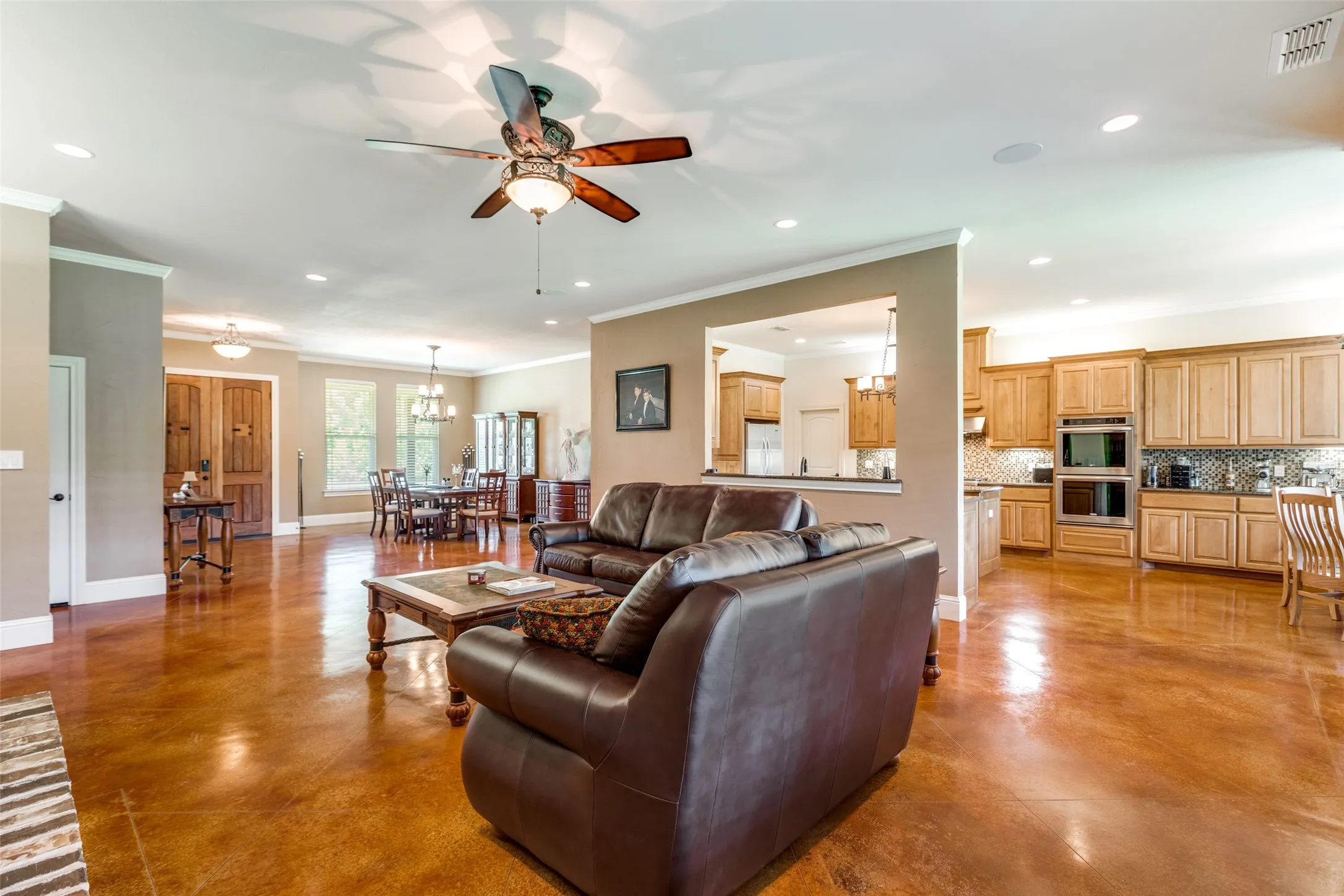 Living room with finished concrete flooring, a chandelier, a ceiling fan, crown molding, and recessed lighting