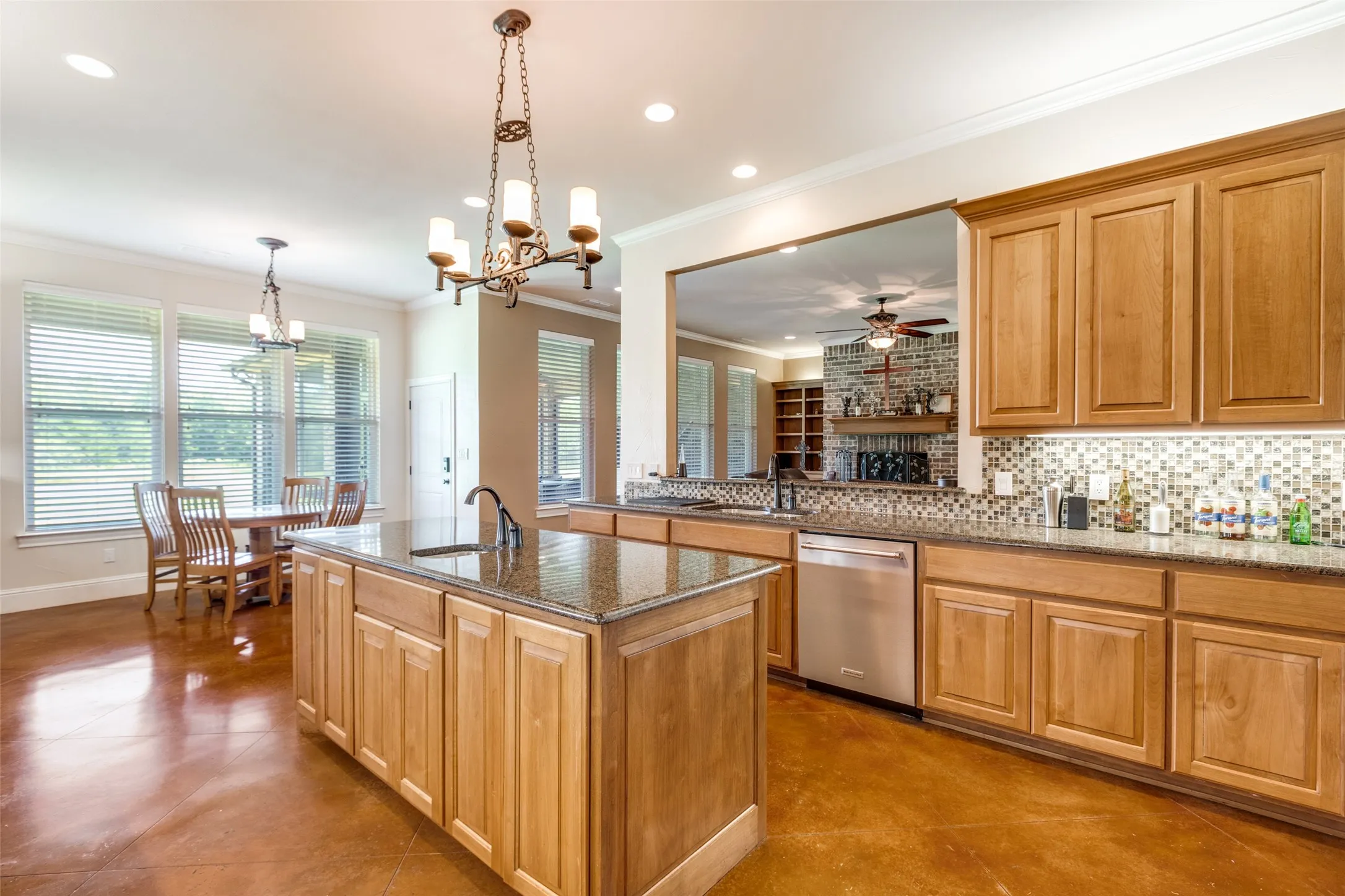 Kitchen with dark stone countertops, crown molding, tasteful backsplash, decorative light fixtures, and healthy amount of natural light