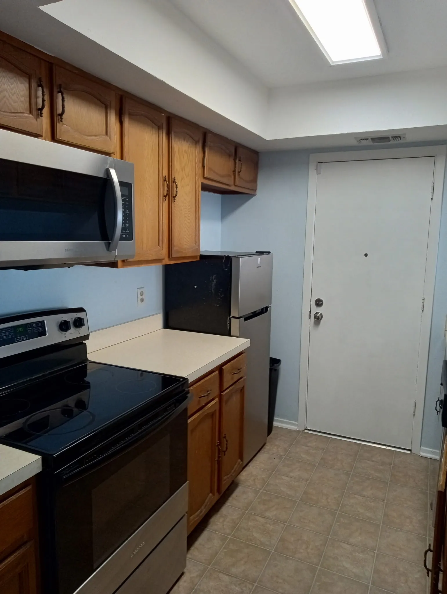 Kitchen featuring stainless steel appliances, wood finish cabinets, and light countertops