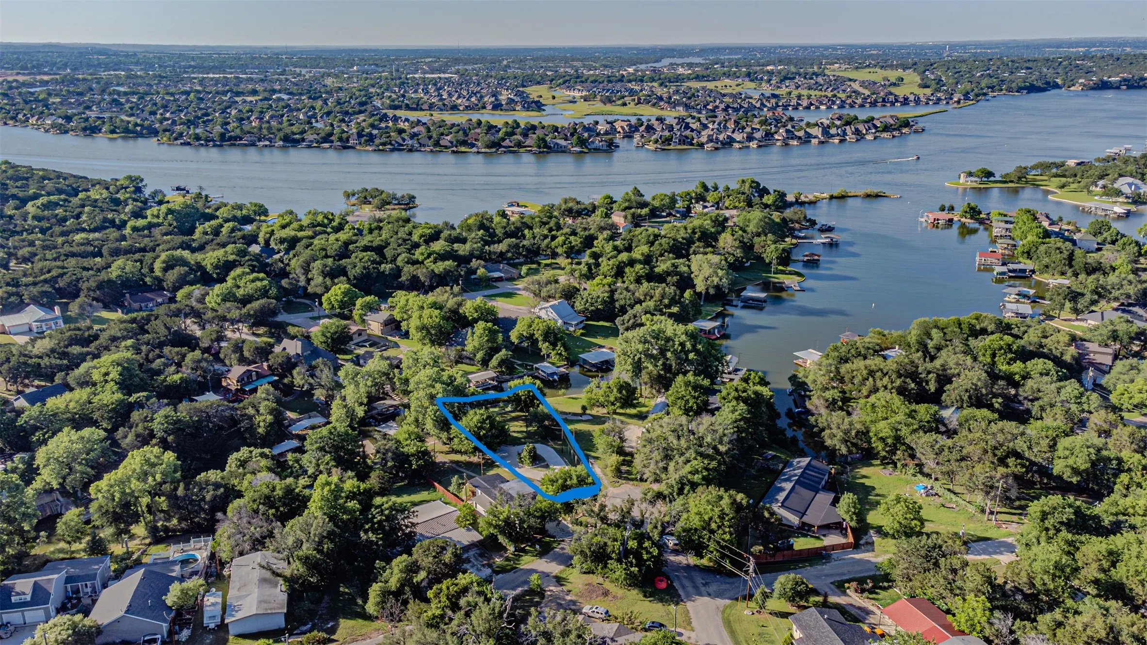 Aerial perspective showcasing a residential property surrounded by mature trees, with a prominent body of water in the background