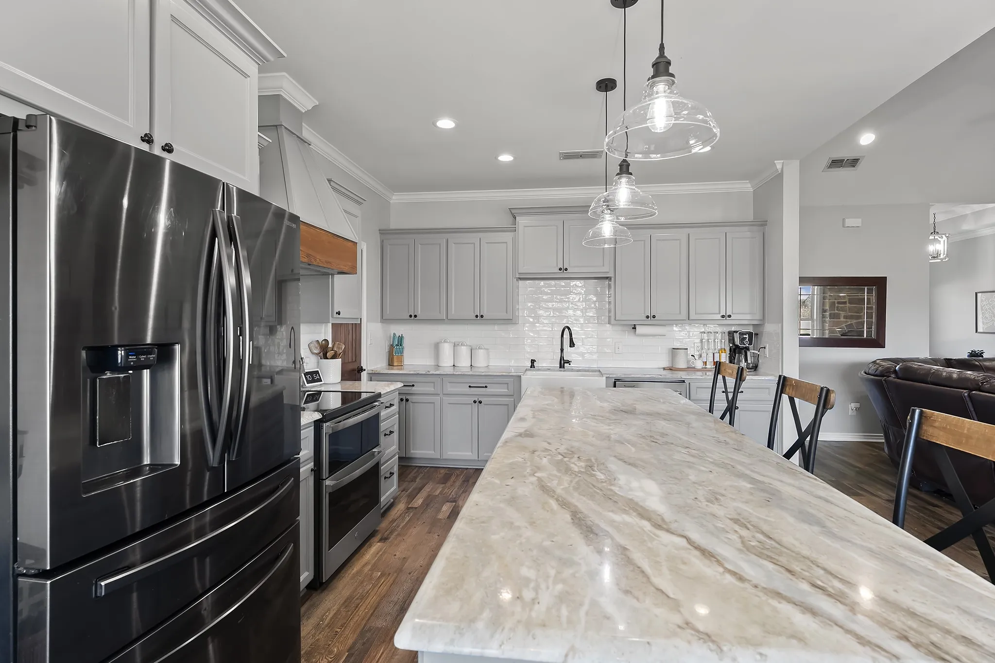 Kitchen with stainless steel appliances, decorative light fixtures, light stone countertops, dark wood-style floors, and crown molding