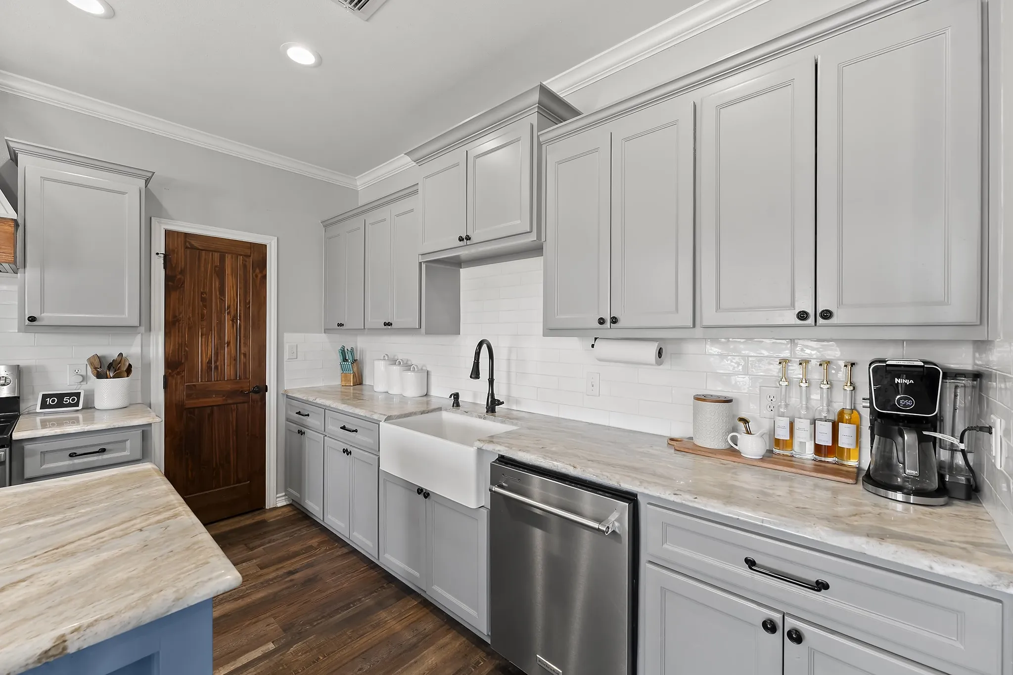 Kitchen featuring dishwasher, ornamental molding, decorative backsplash, light stone counters, and dark wood-style floors