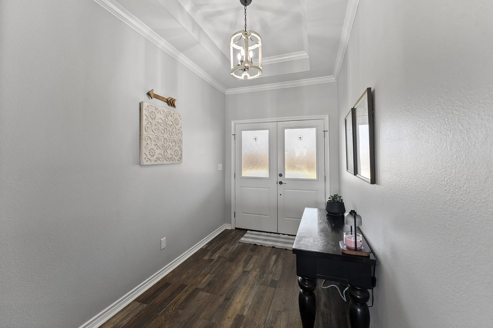 Entryway with a raised ceiling, wood finished floors, a chandelier, and crown molding