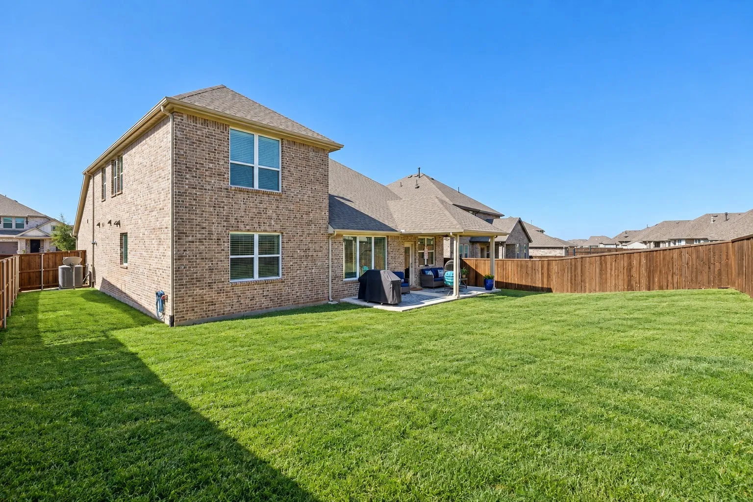 Expansive grassy lawn with a covered patio, full privacy fencing, and a brick exterior