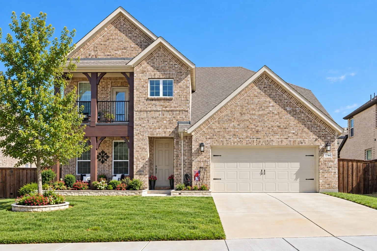Brick-clad exterior with a two-car garage, a second-story balcony with metal railing, and a covered ground-level porch