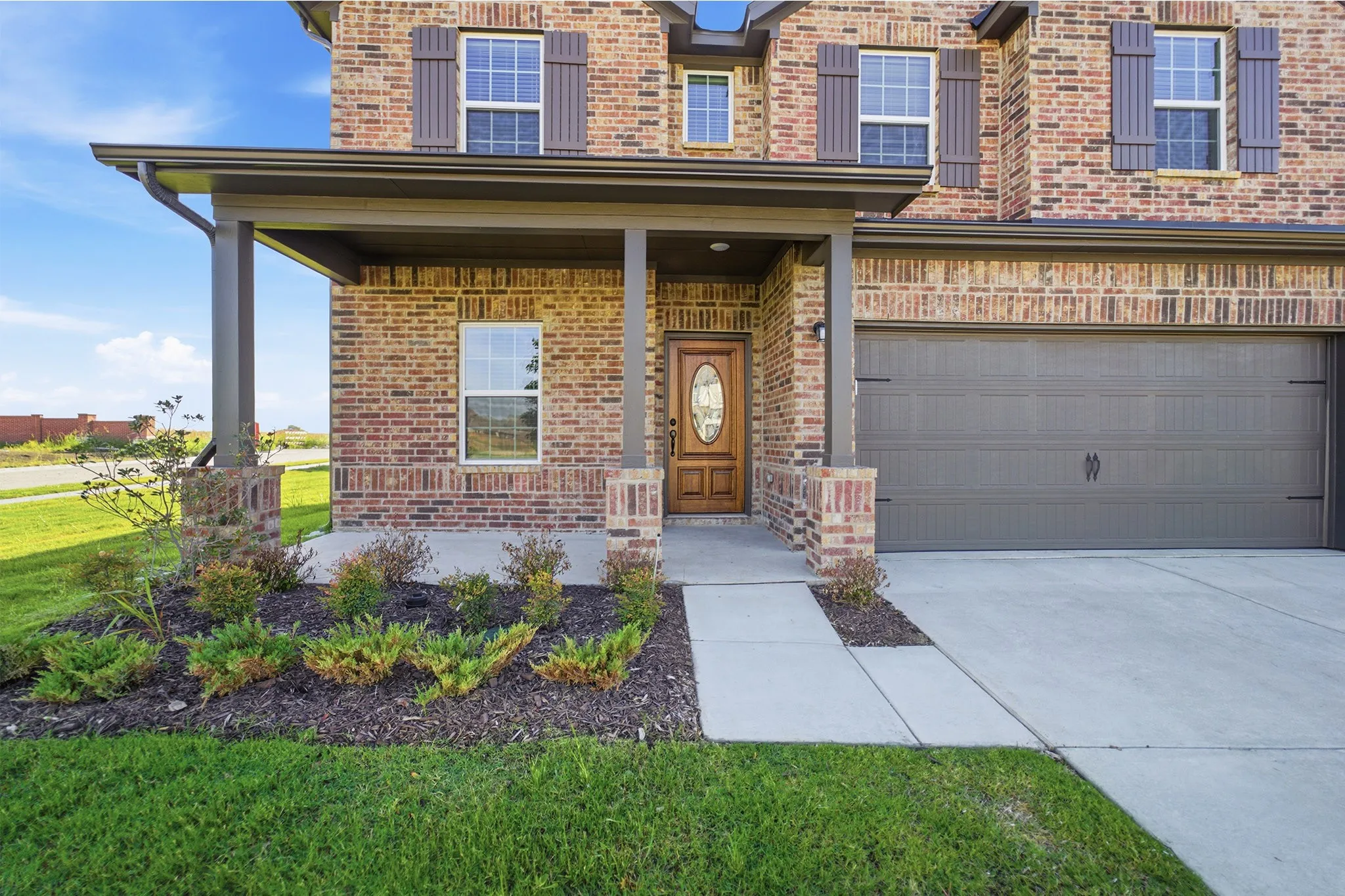 Brick exterior featuring a covered front porch with substantial columns, a wood-finish entry door with an oval glass insert, and decorative window shutters