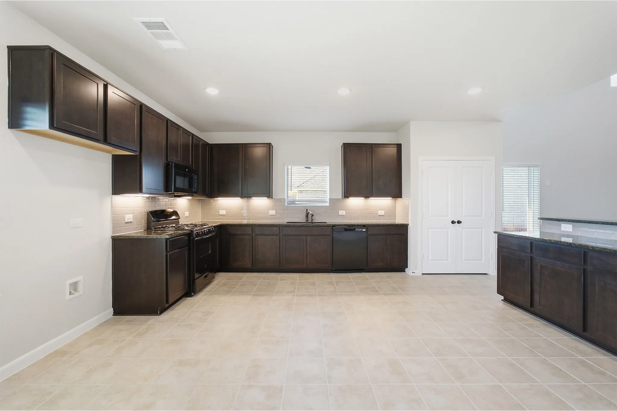 Kitchen featuring dark wood cabinetry, light-toned tile flooring, black appliances, and recessed lighting