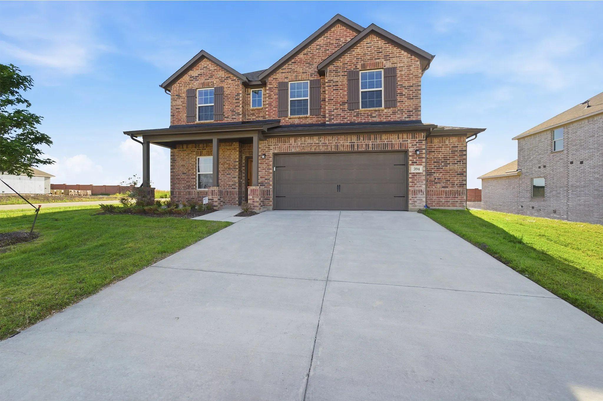 Two-story brick exterior featuring a covered front porch, an attached two-car garage, and a concrete driveway