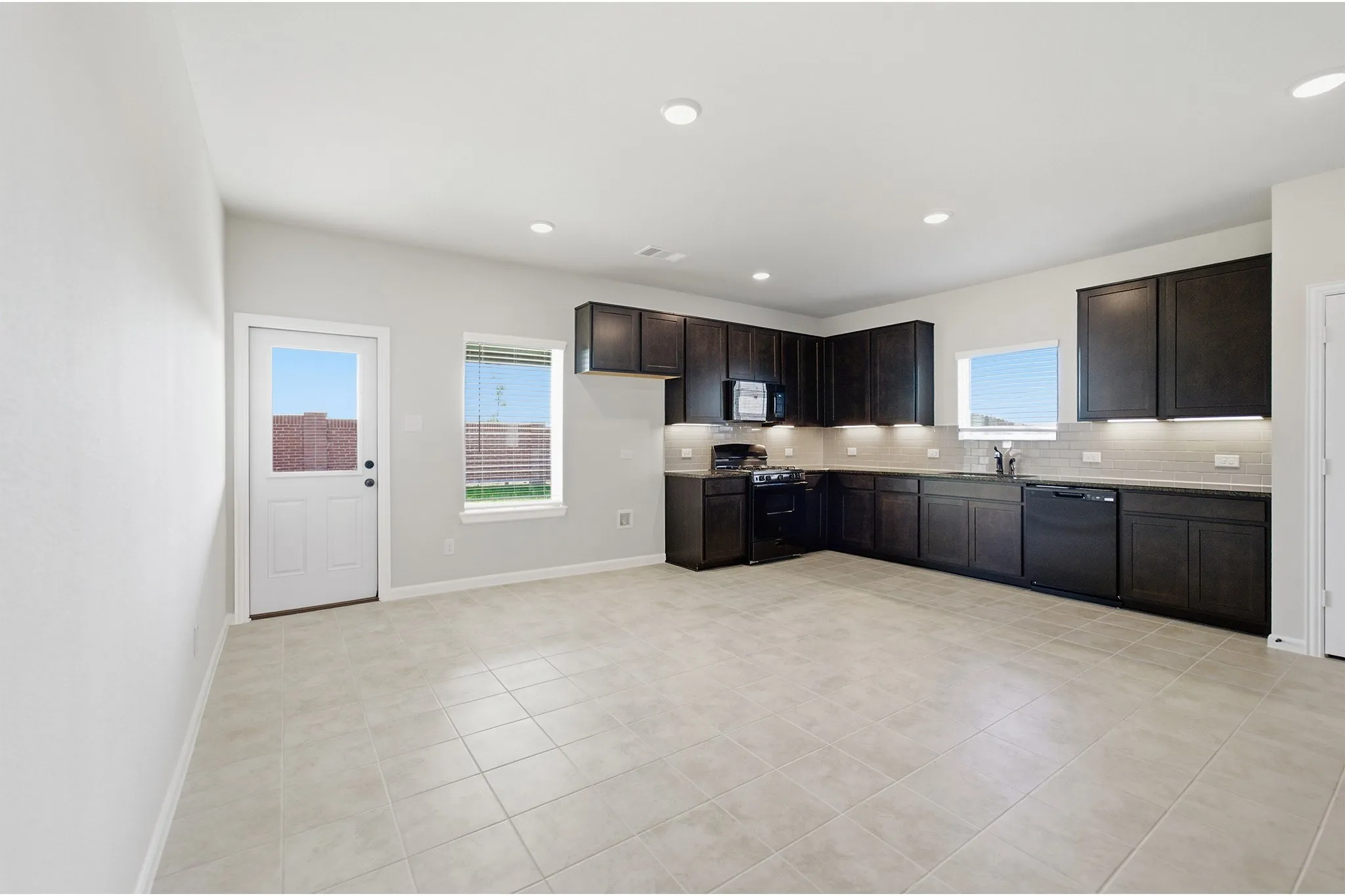 Spacious kitchen featuring dark wood cabinetry, solid surface countertops, a full suite of black appliances, and recessed lighting