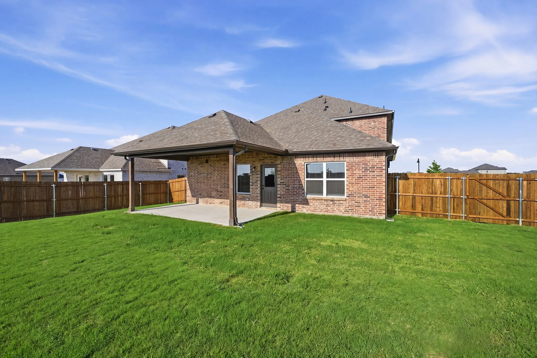 Expansive green lawn with a covered patio, brick exterior, and a privacy fence