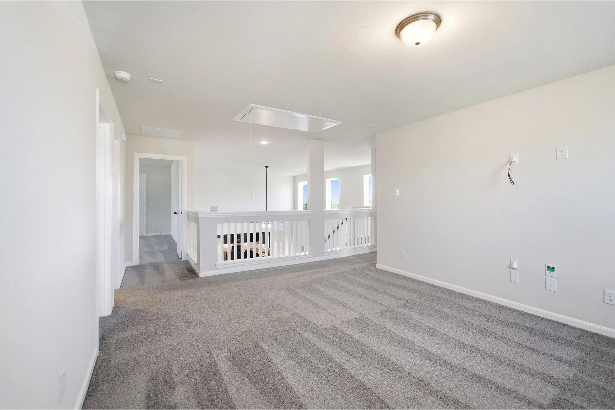 Carpeted loft area with white wall finishes, semi-flush mount lighting, and a white balustrade overlooking a lower level