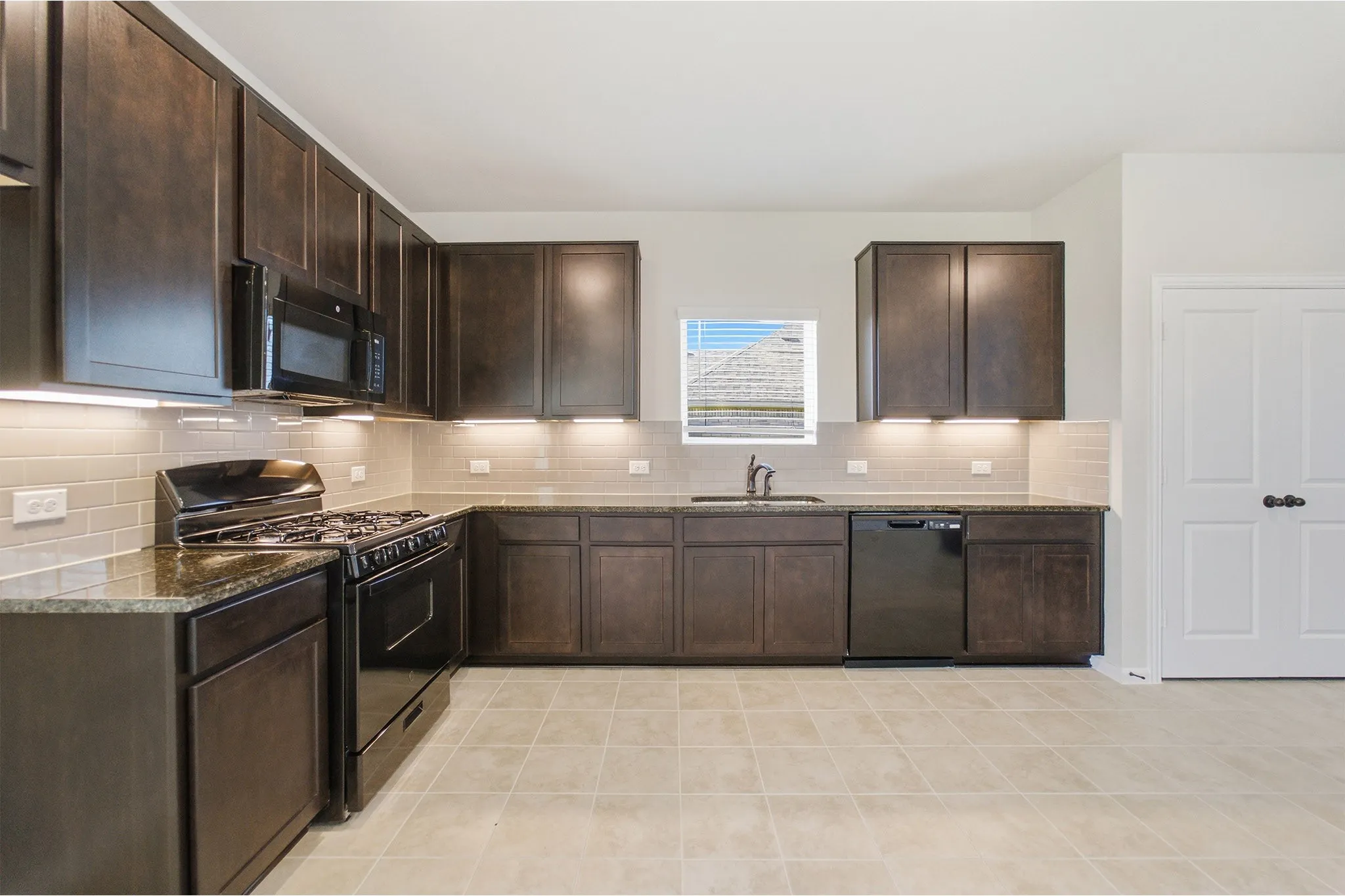 Open-concept kitchen featuring dark wood cabinetry, granite countertops, a subway tile backsplash, and black appliances including a gas range, microwave, and dishwasher