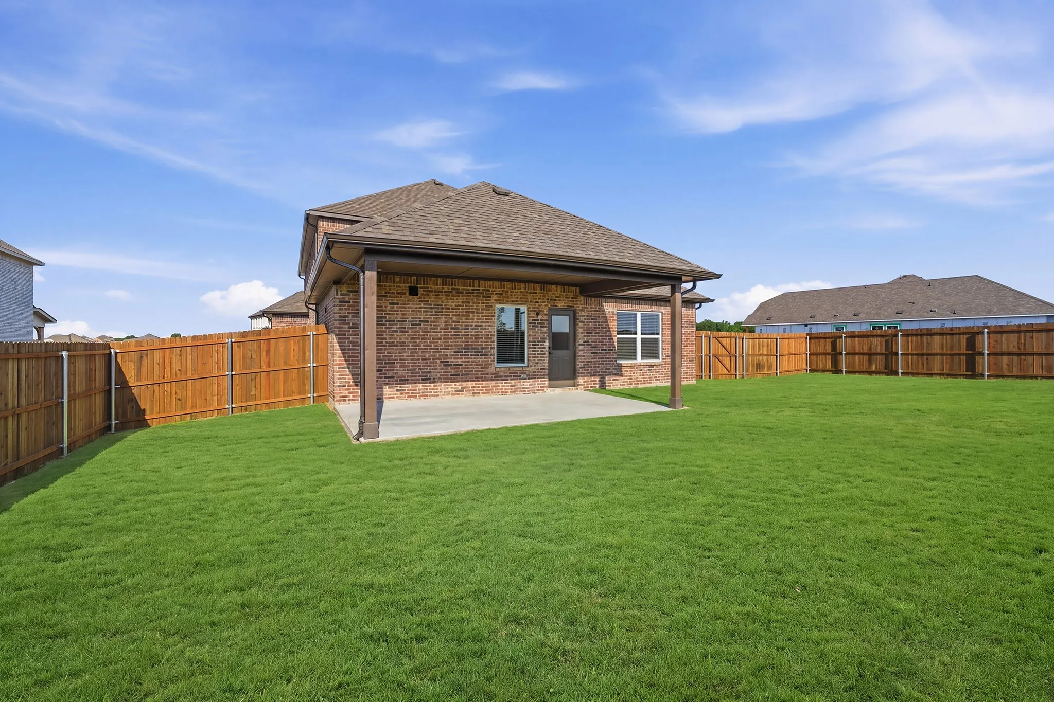 Spacious backyard featuring a covered patio, extensive green lawn, privacy fencing, brick exterior, and a shingle roof