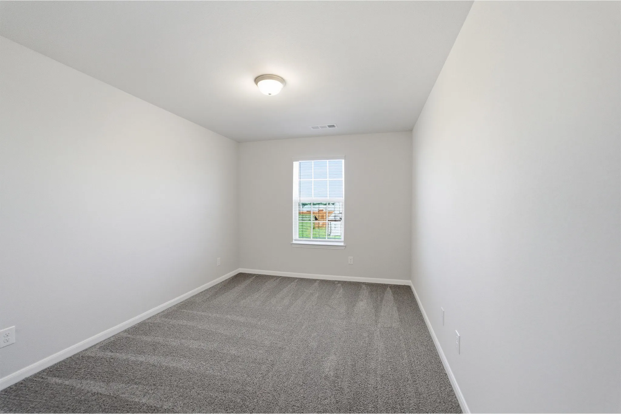 Bright room featuring a window with grid panes, neutral gray carpeting, a flush-mount ceiling light fixture, and white painted walls