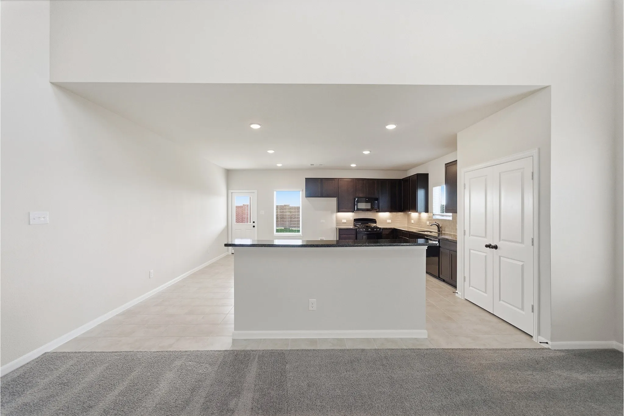 Open-concept living space featuring a kitchen with dark cabinetry, black countertops, and stainless steel appliances