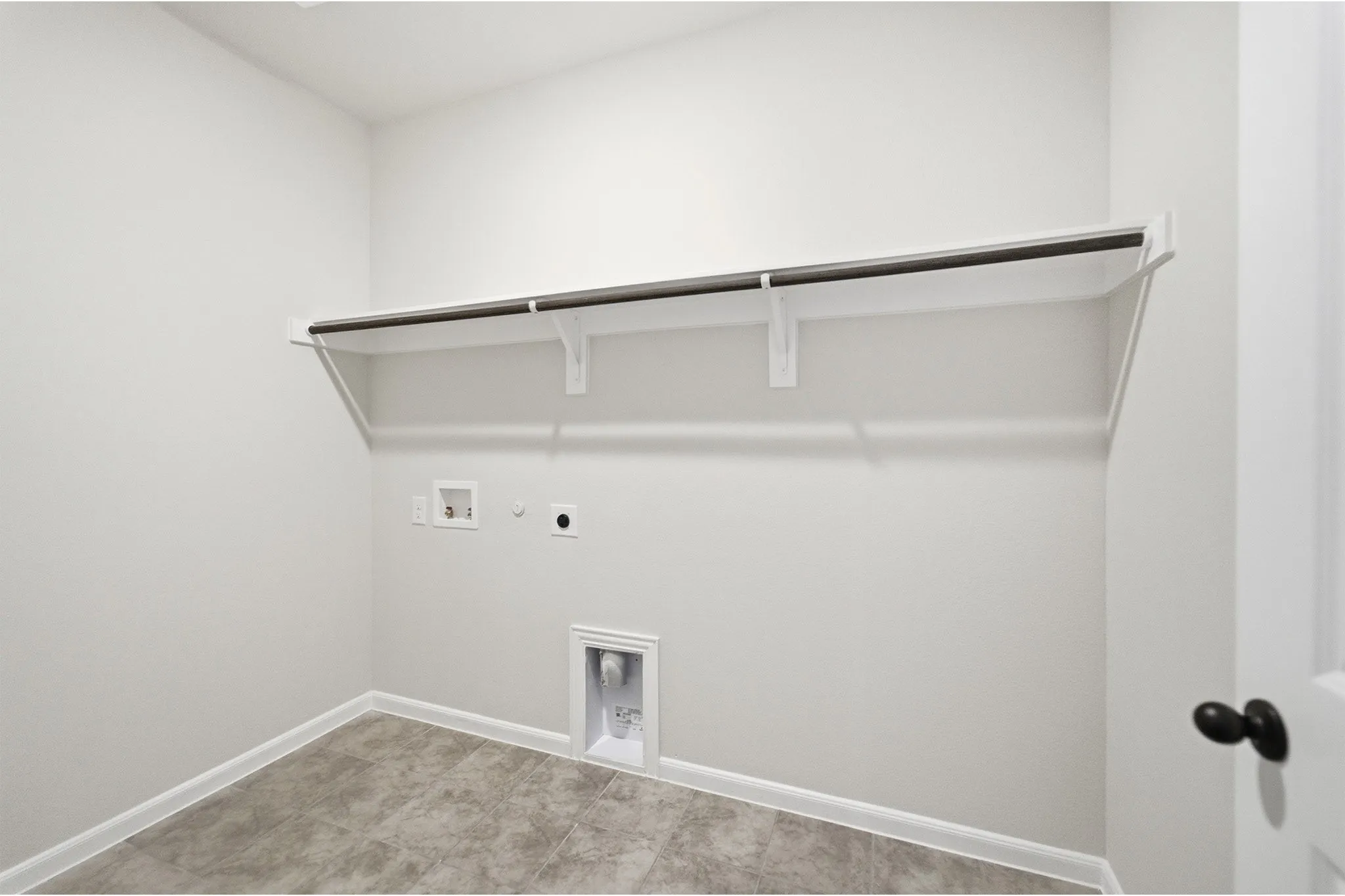 Dedicated utility space featuring a built-in shelving unit with hanging rod, durable tile flooring, and essential appliance hookups