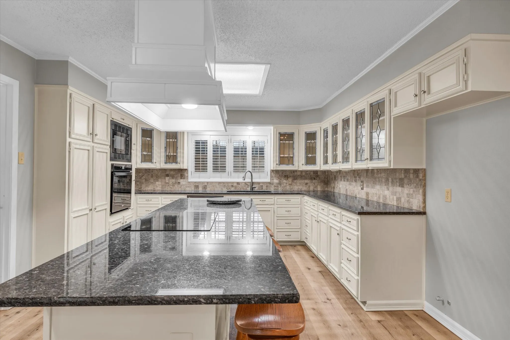 Kitchen with black appliances, a center island, a textured ceiling, backsplash, and light wood finished floors