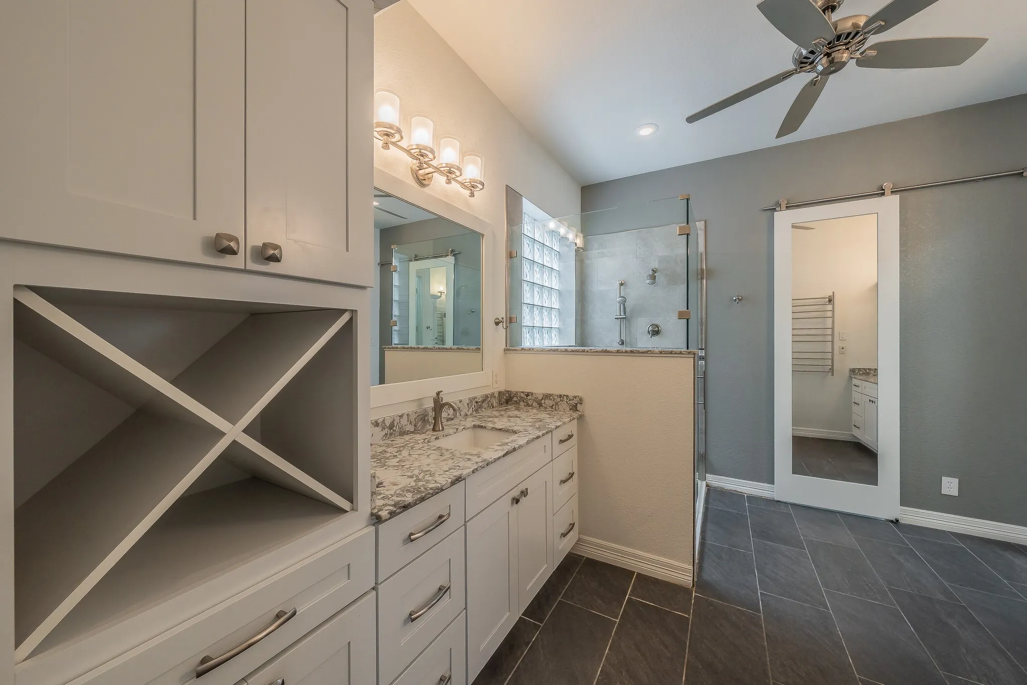 Bathroom featuring a vanity with a granite-style countertop, white cabinetry with silver hardware, and a glass-enclosed shower with glass block window