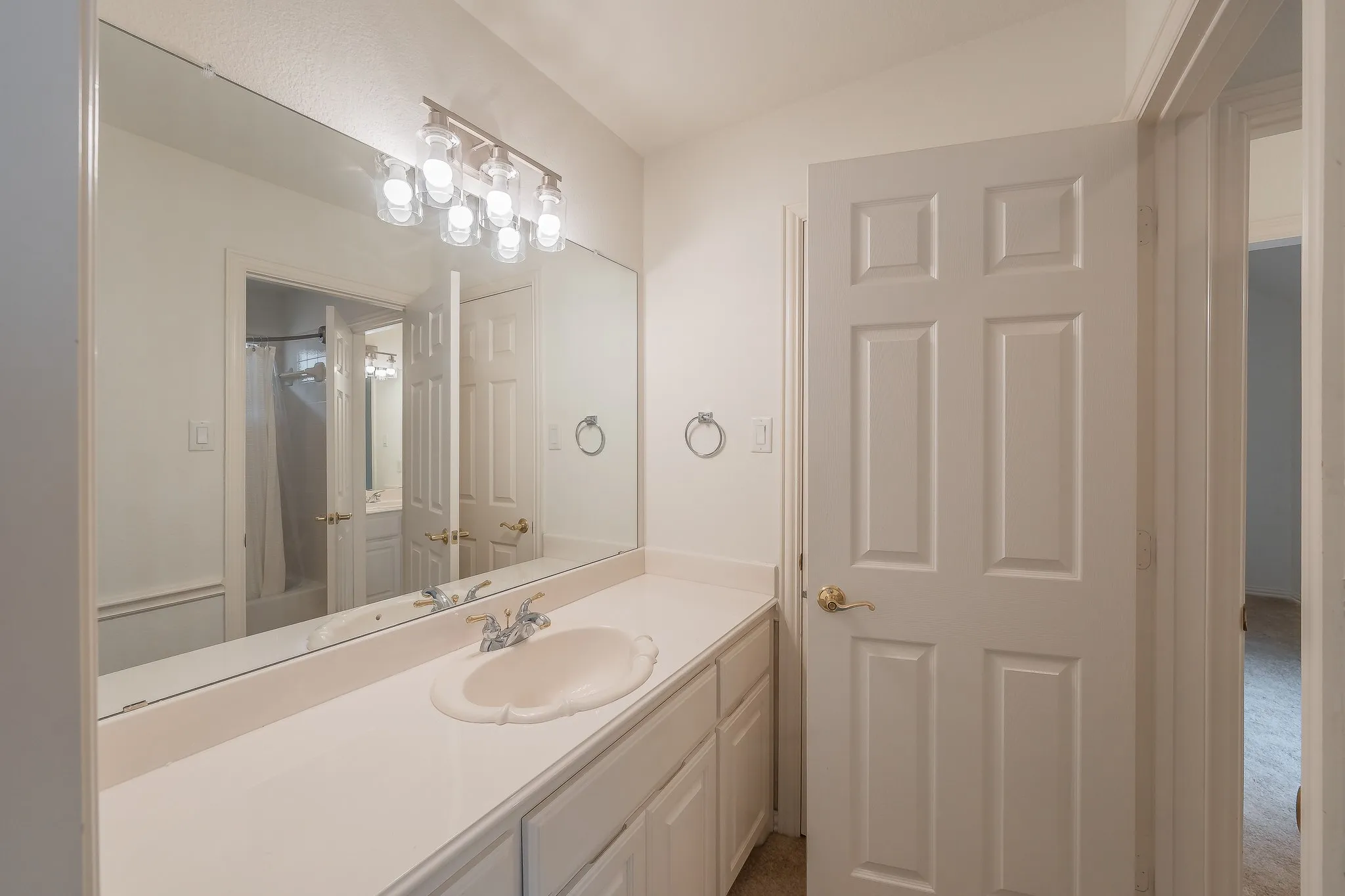 White vanity with an integrated sink, polished chrome faucet, and expansive wall-mounted mirror with new four-light fixture connecting the Jack & Jill bedrooms