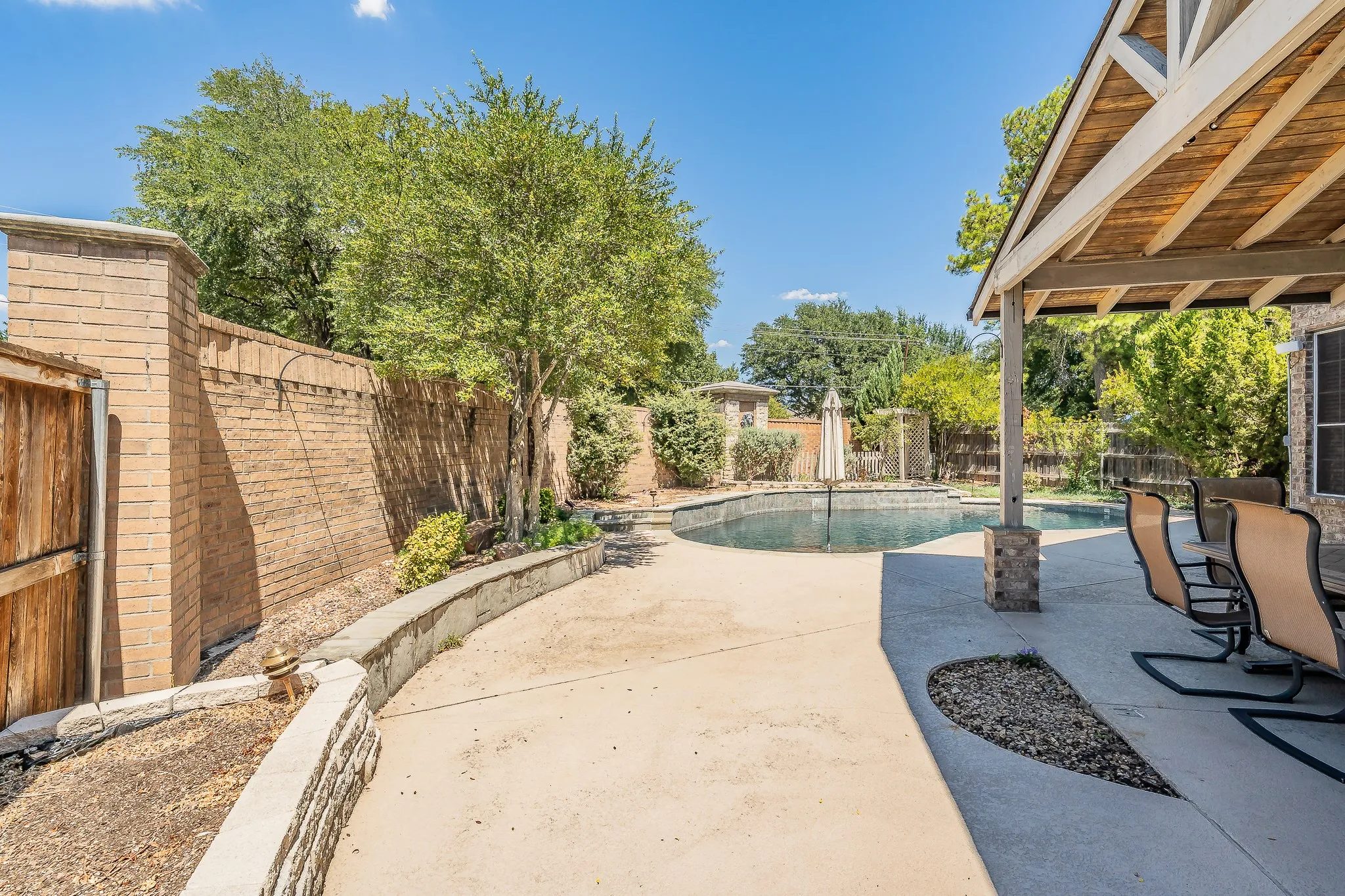 Shaded patio area with concrete surfacing, adjacent to a built-in swimming pool