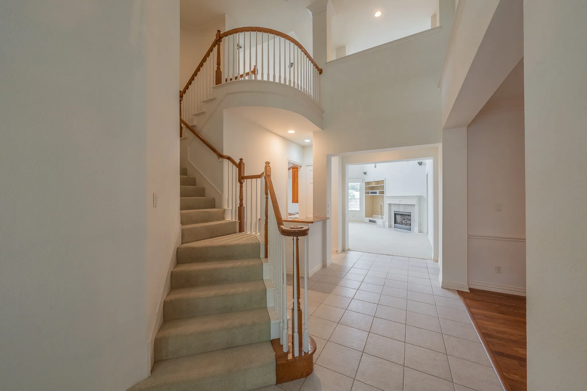 Two-story foyer featuring a curved staircase with wood-finish railing, a second-story balcony, and tile flooring