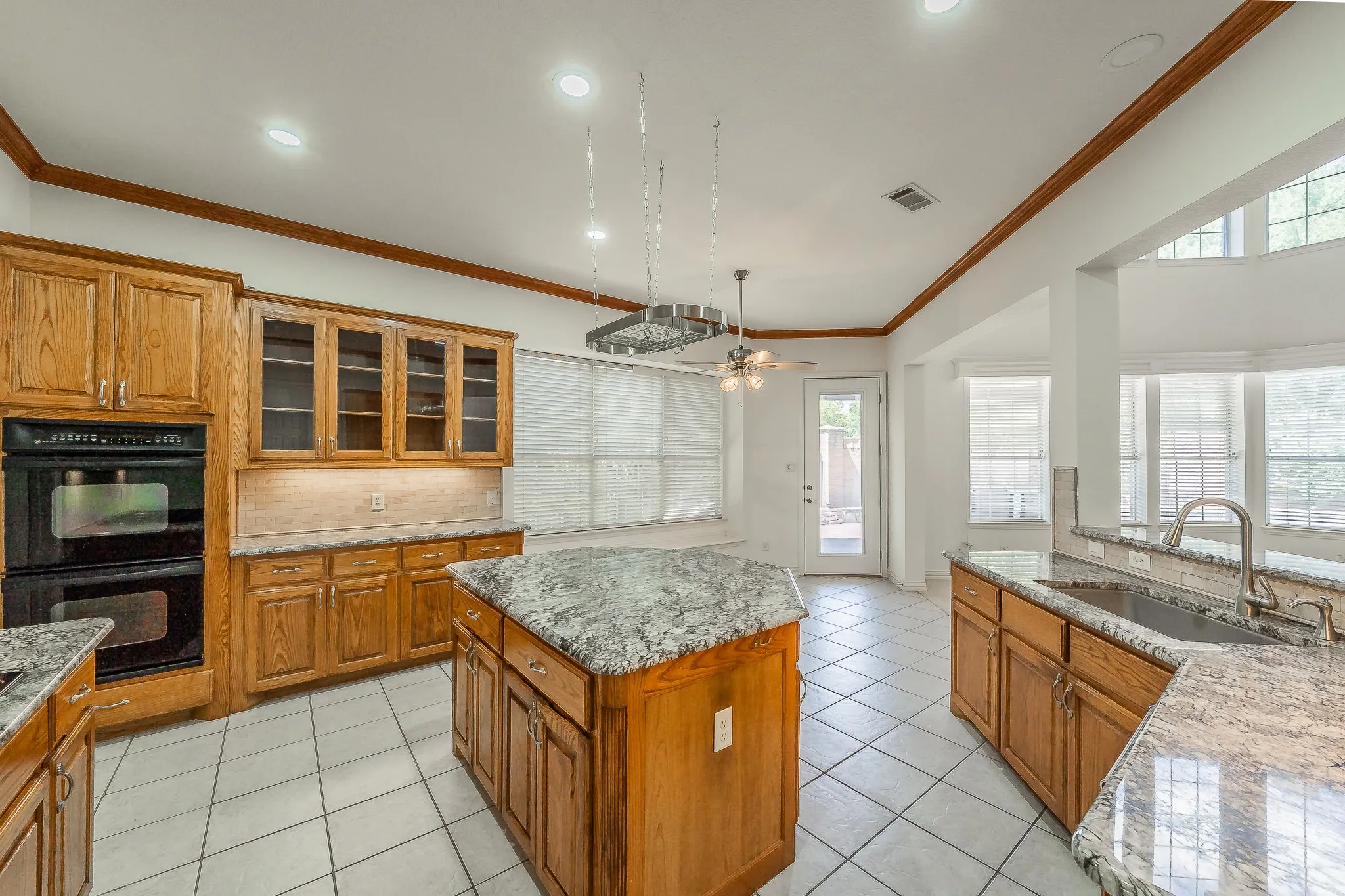 Kitchen featuring wood cabinetry, granite countertops, a central island, and white tile flooring