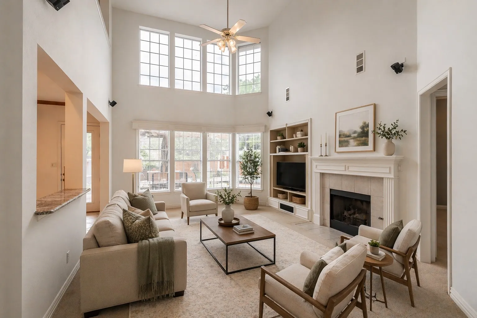AI staging shows spacious living area featuring a two-story ceiling, multiple large windows, a built-in media center with shelving, a fireplace with a detailed mantel, and a granite-topped pass-through