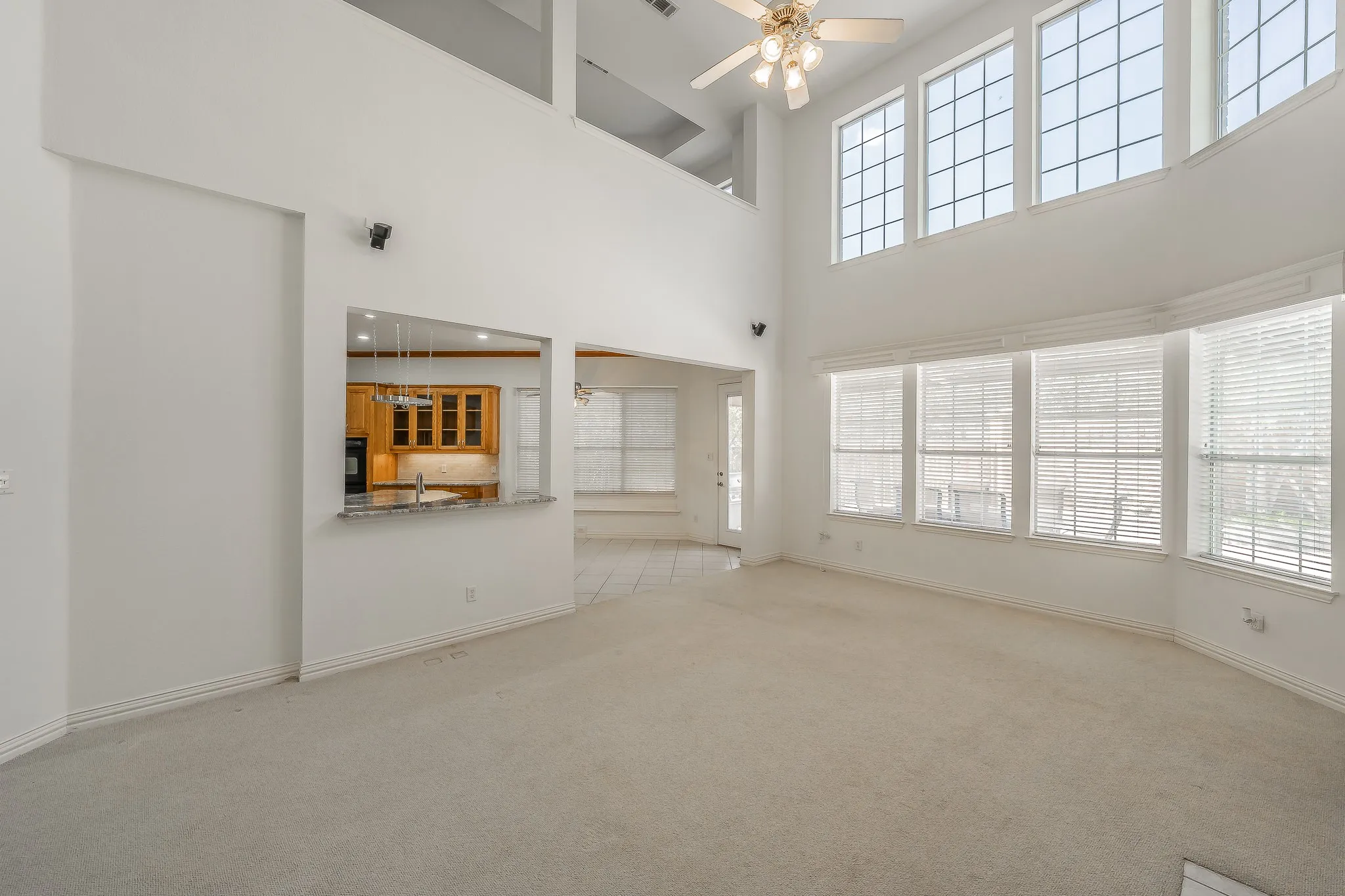 Vaulted ceiling, multiple large windows, ceiling fan, pass-through opening, and wood-finish cabinetry