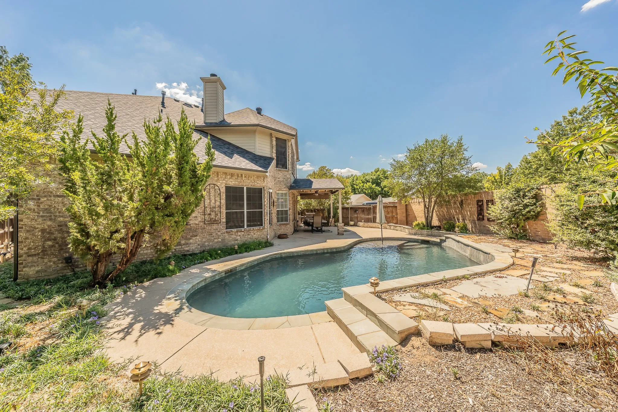 In-ground swimming pool with concrete decking, brick exterior, and covered patio