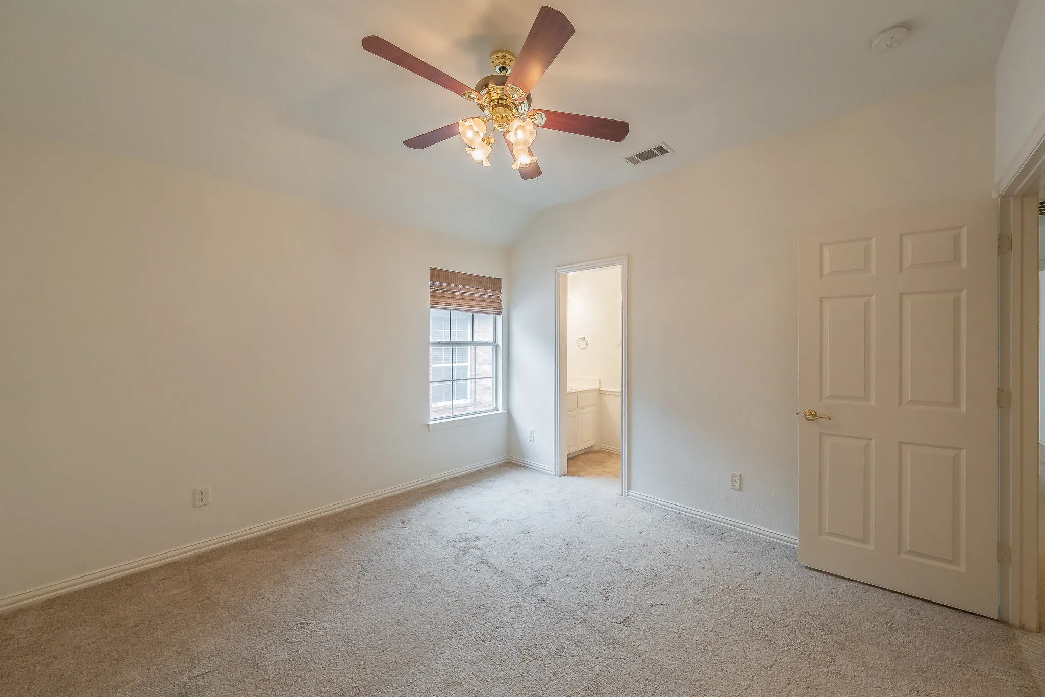 Carpeted interior room featuring a vaulted ceiling with a decorative ceiling fan, a window with a woven wood shade, and a paneled interior door