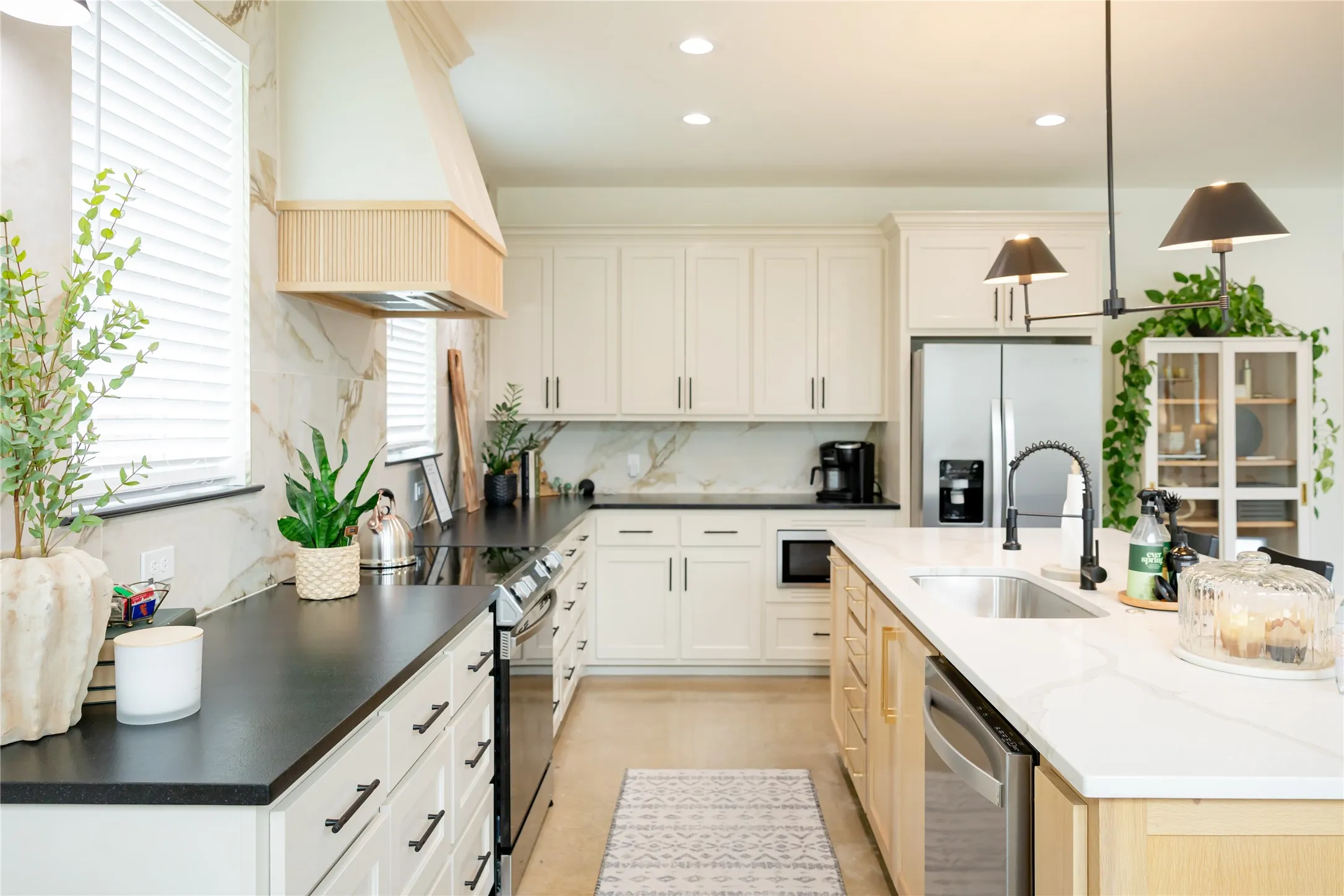 Kitchen with pendant lighting, stainless steel appliances, two tone cabinets, an island with sink, and decorative backsplash