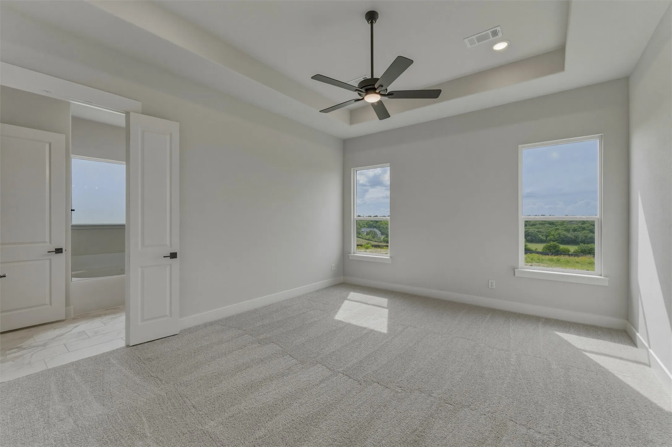Spacious room featuring dual windows, tray ceiling, and a modern ceiling fan