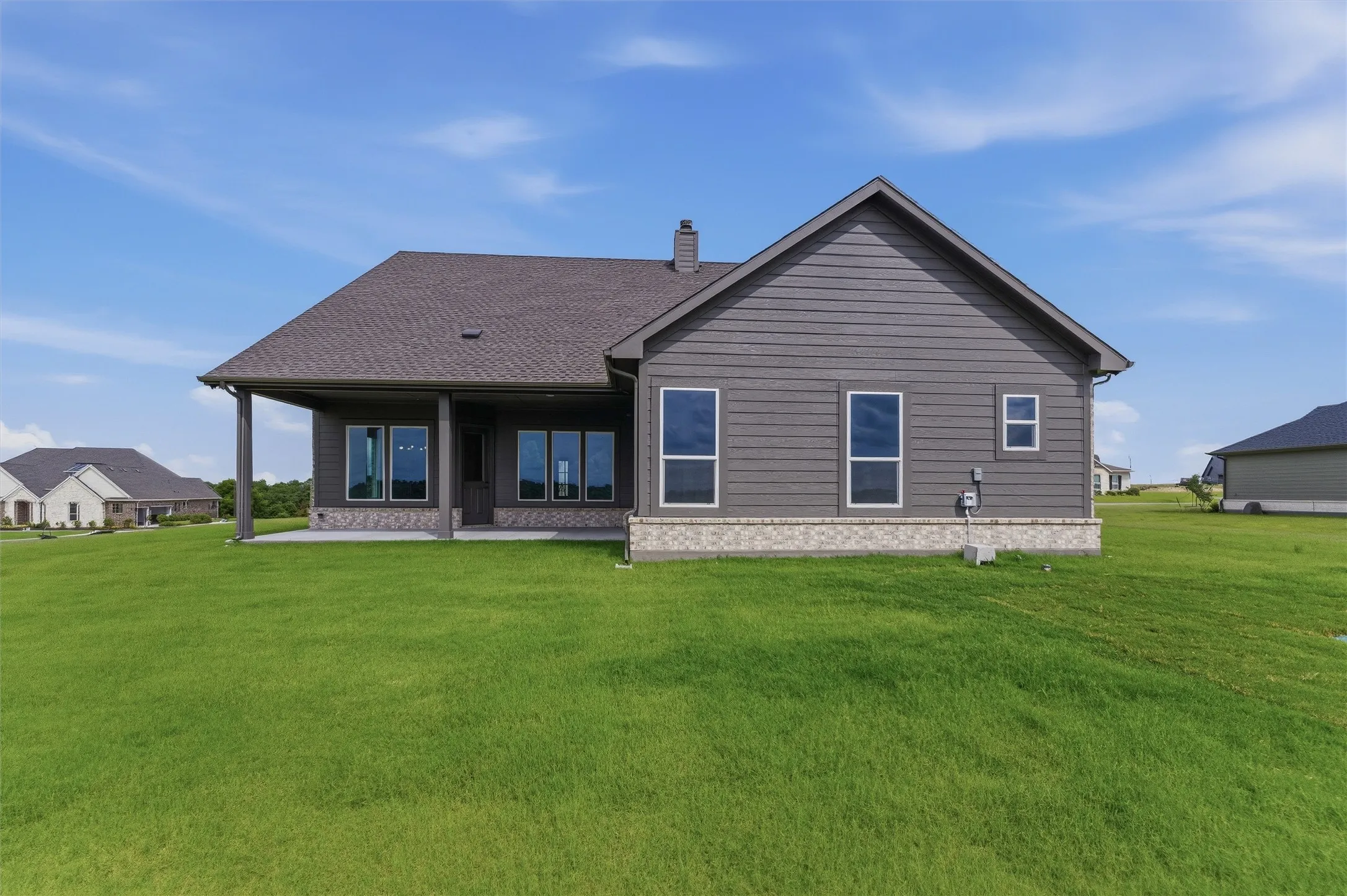Expansive green lawn bordering a single-story residence with dark gray siding and a light-colored stone accent foundation