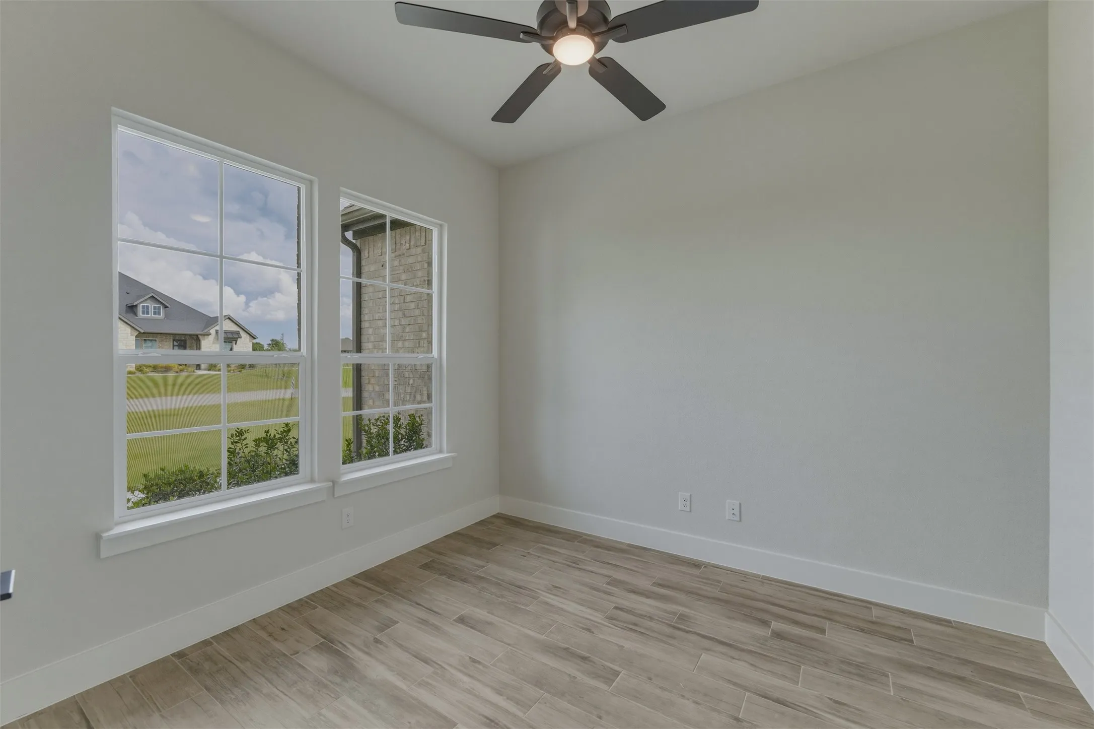 Light-filled room featuring two multi-pane windows, wood-finish flooring, a ceiling fan with integrated lighting, and neutral wall tones