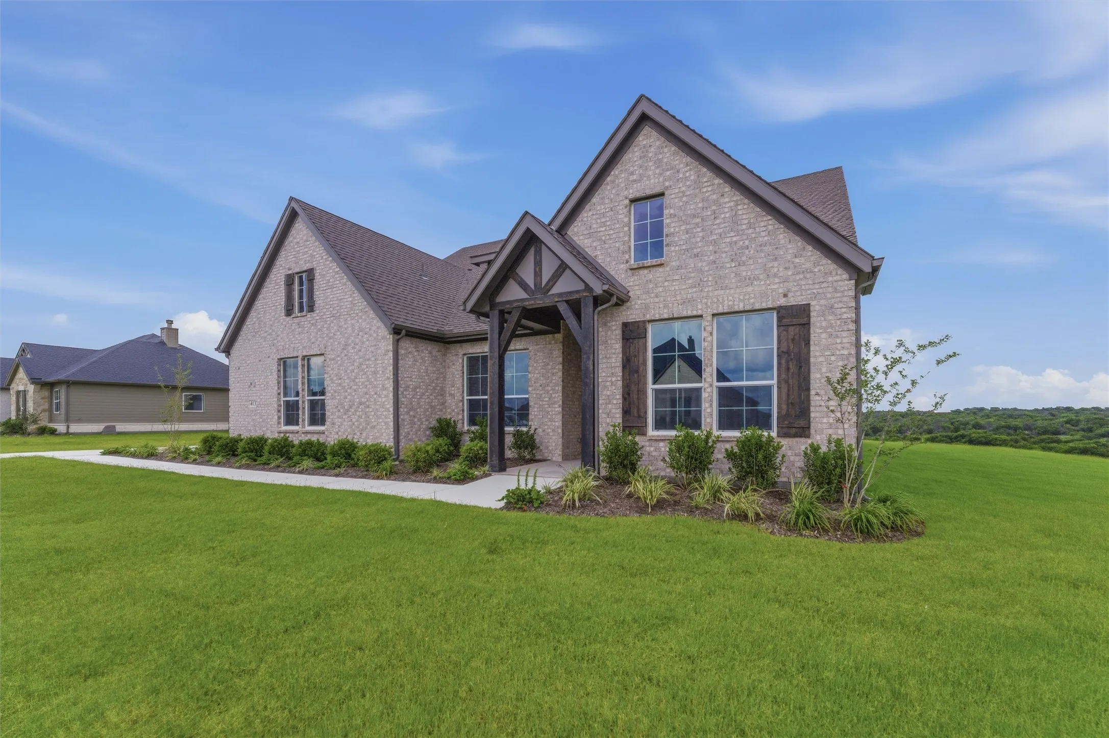 New construction home featuring a light-colored brick exterior, dark gabled roofing, and a prominent dark wood entry porch