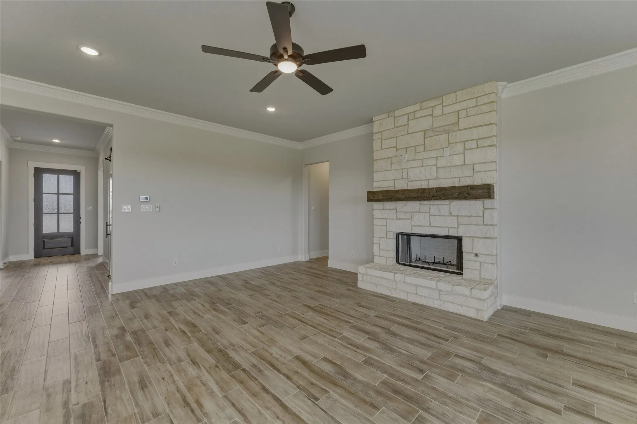 Living space featuring a stone-clad fireplace with wood mantel, wood-finish flooring, recessed lighting, crown molding, and a ceiling fan