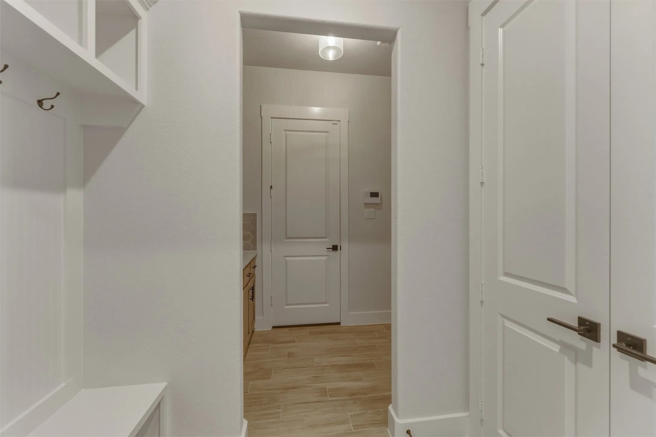 Entryway featuring built-in storage with coat hooks, white paneled doors with bronze hardware, and wood-finish tile flooring
