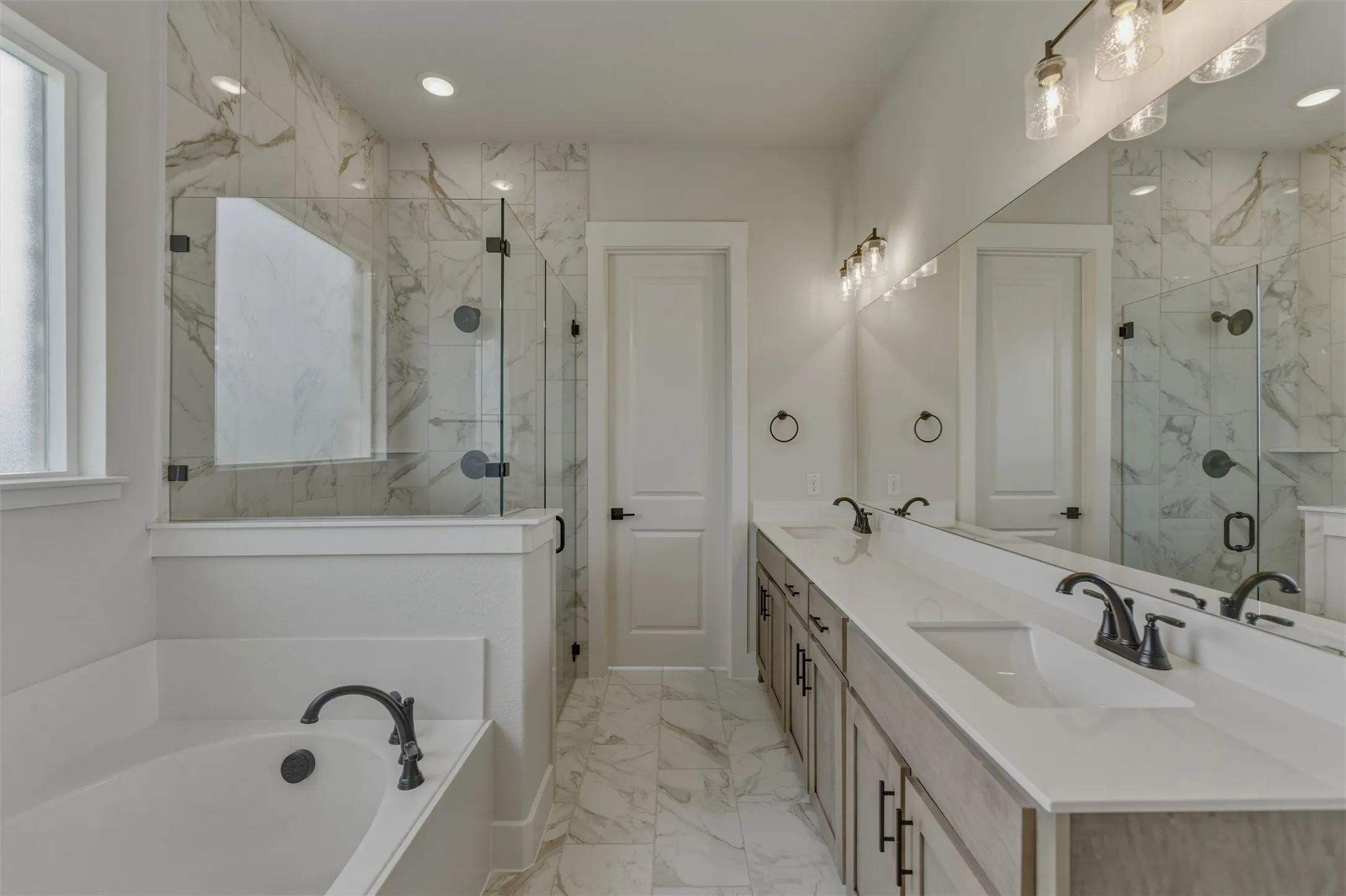 Contemporary bathroom featuring a spacious built-in tub, a walk-in shower with clear glass enclosure and marble-look tile surround, a dual vanity with undermount sinks, and an expansive mirror