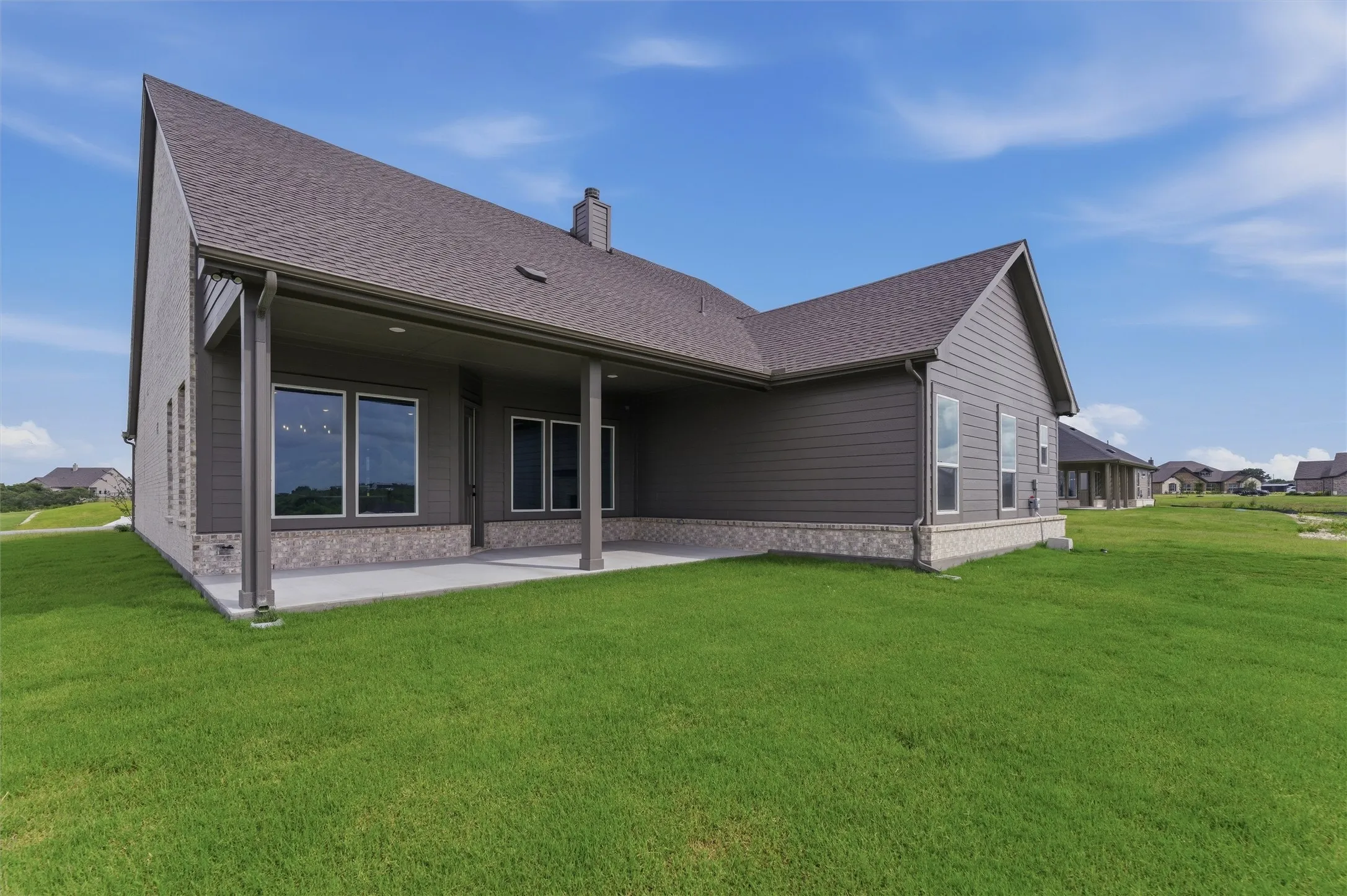 Expansive green lawn surrounds a residence featuring a covered patio with gray siding and stone wainscoting
